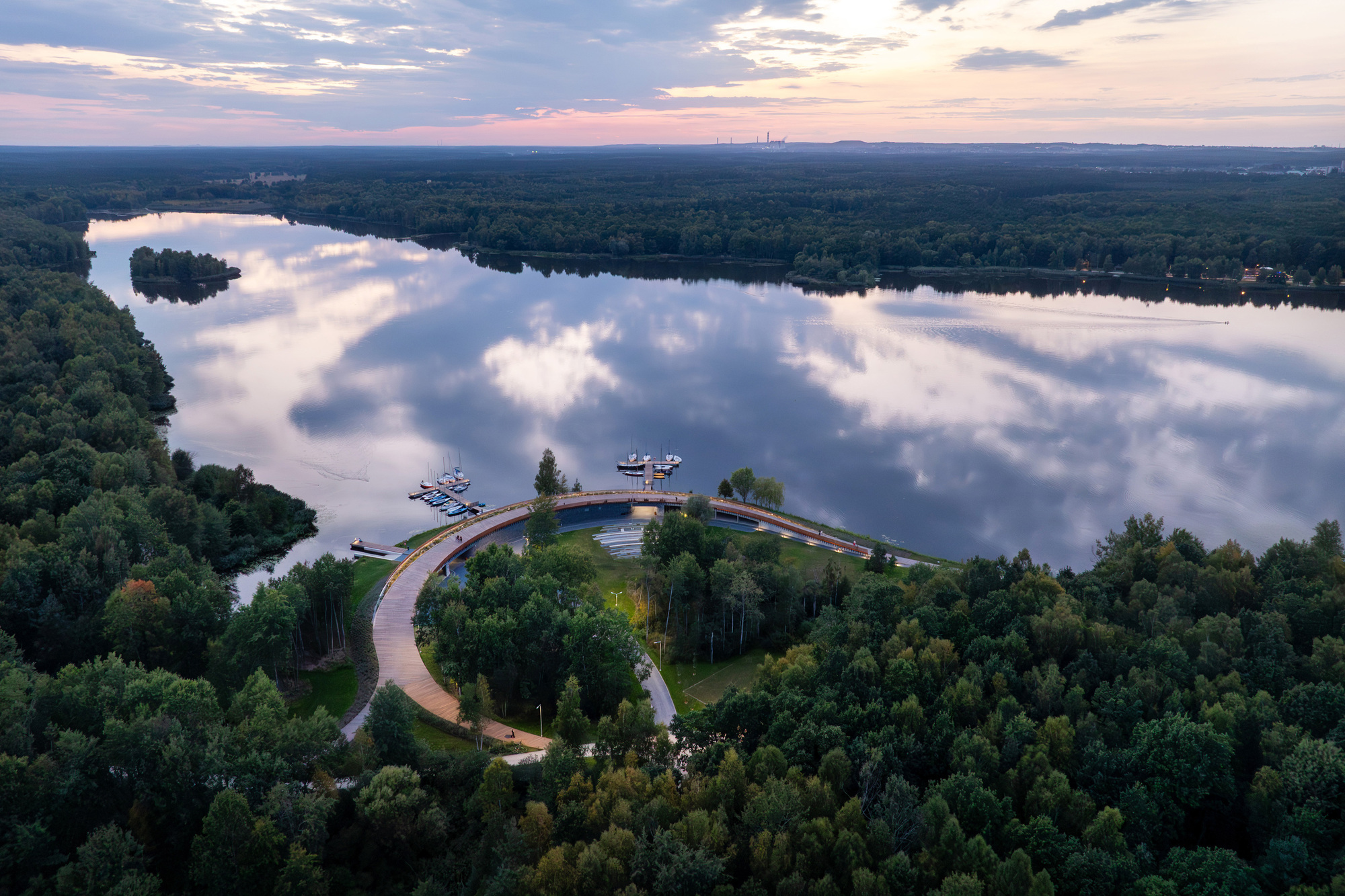 Drone view of the looping timber bridge crossing the lake at dusk with clouds reflected in calm water