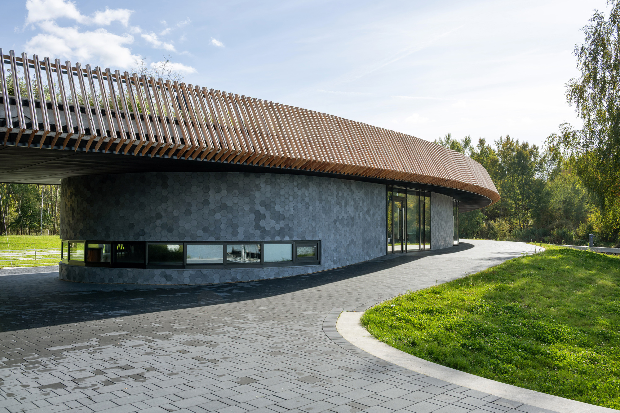 Ground view of the dark concrete facade with slatted copper roof and ribbon windows along paved walkway