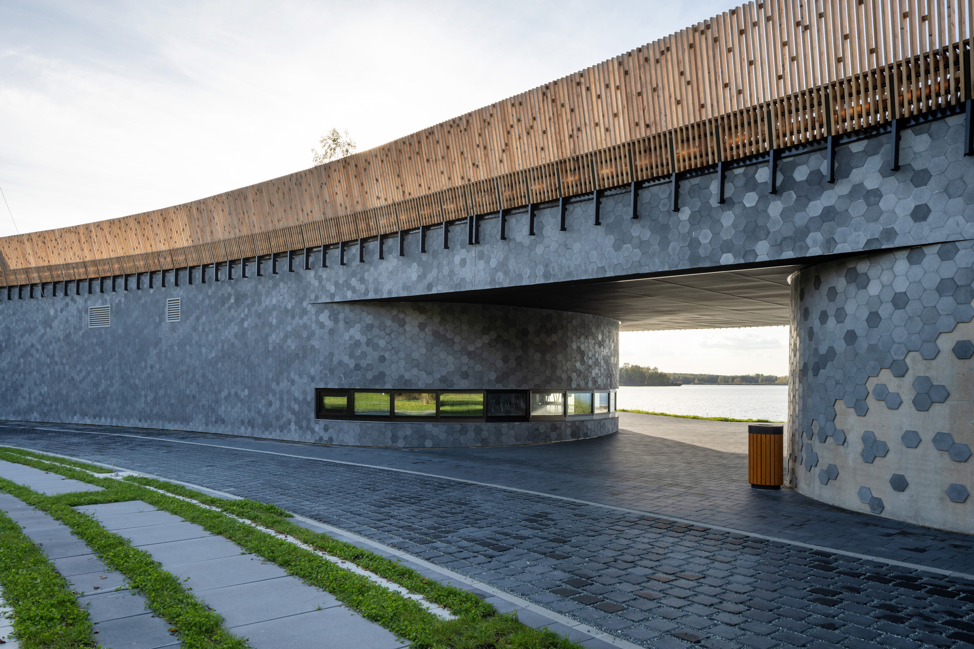 Covered entry courtyard with hexagonal tile concrete walls and vertical timber screen above under overcast sky