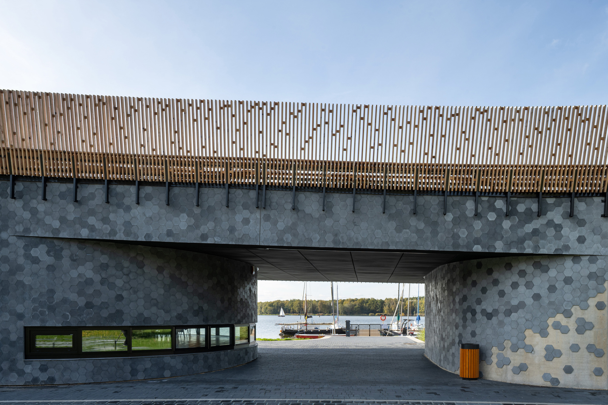 Portal view through hexagonal tiled concrete walls framing sailboats at the marina beyond