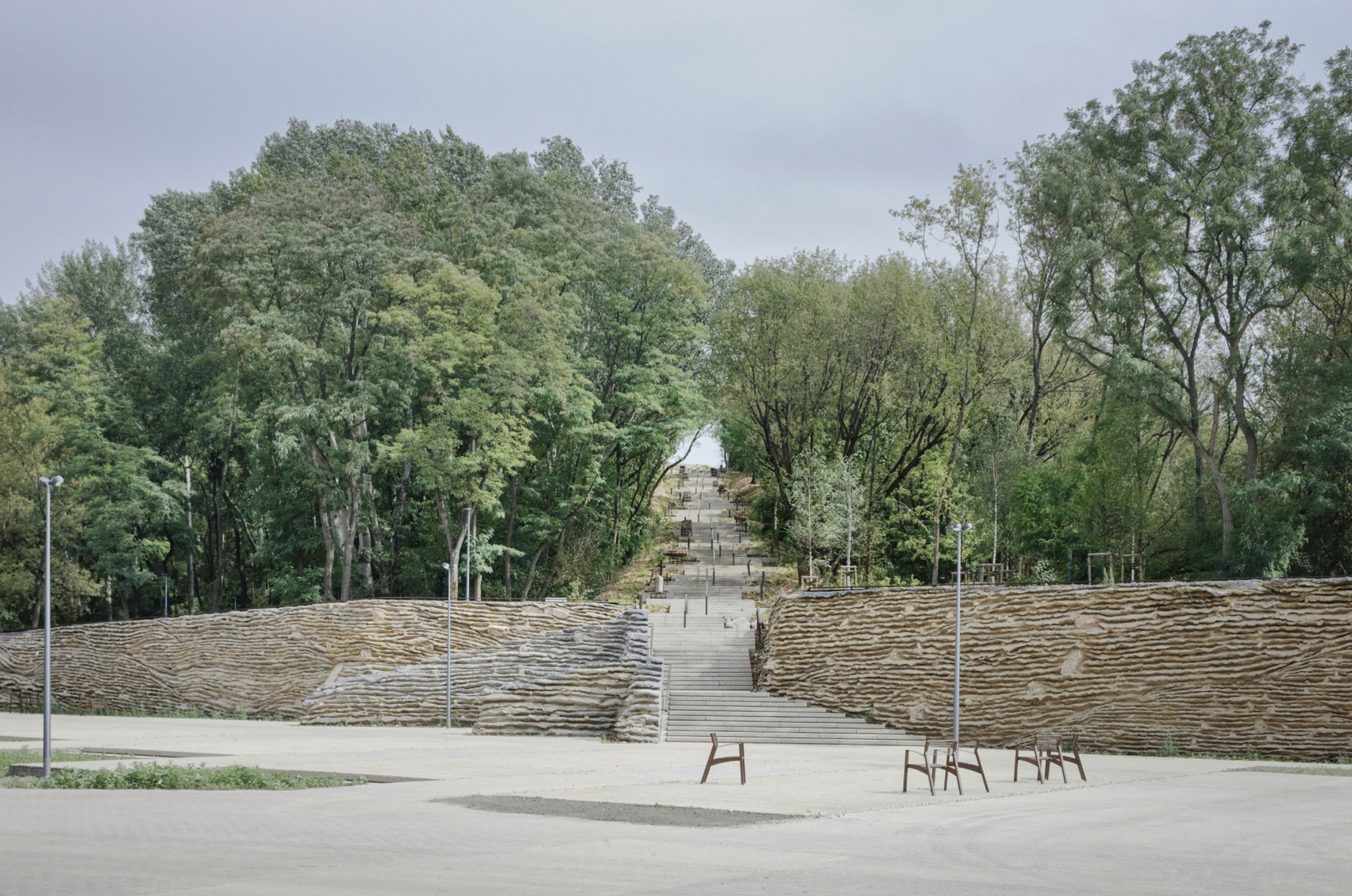 Outdoor amphitheater with timber-stepped seating banks flanking a central staircase under an overcast sky