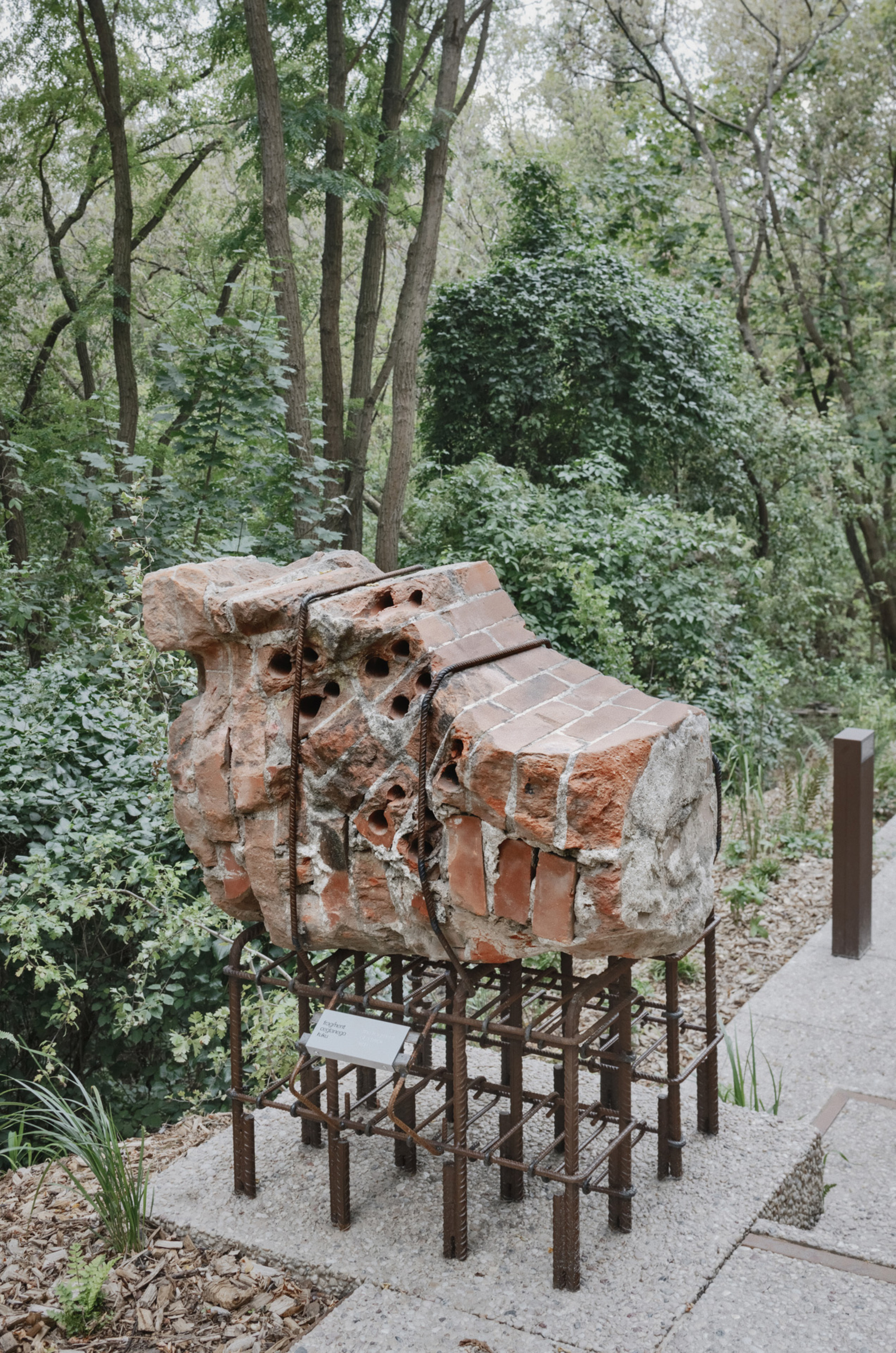 Brick kiln fragment displayed on a steel rebar armature beside a forest path