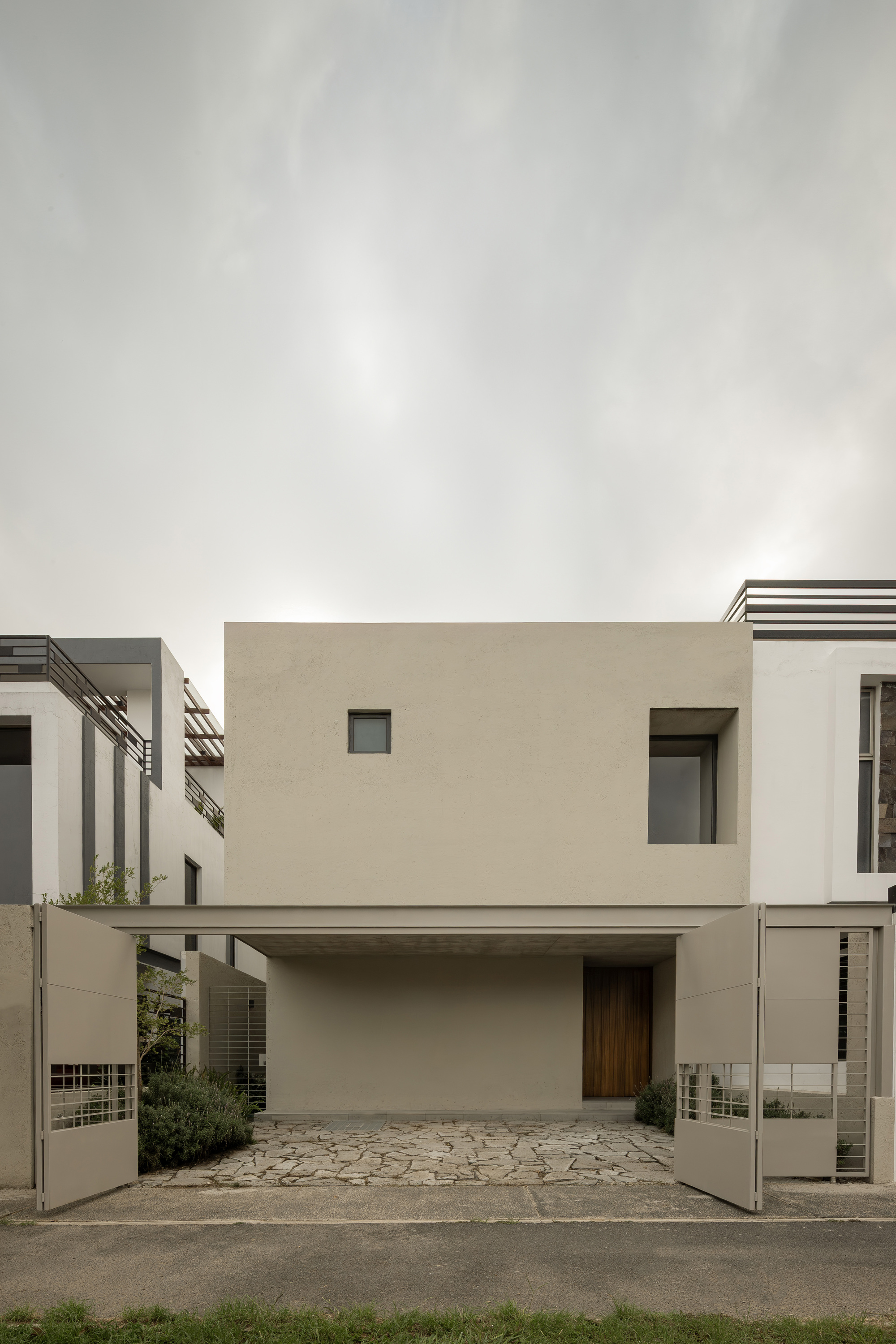 Street facade with recessed carport and cantilevered upper volume in smooth stucco under overcast sky
