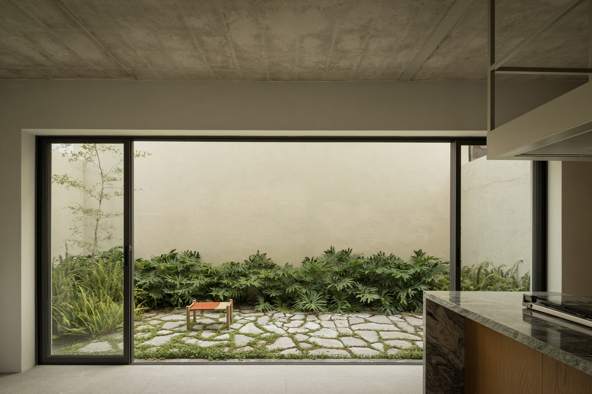 Kitchen view through sliding glass doors to stone-paved courtyard garden with low planted beds
