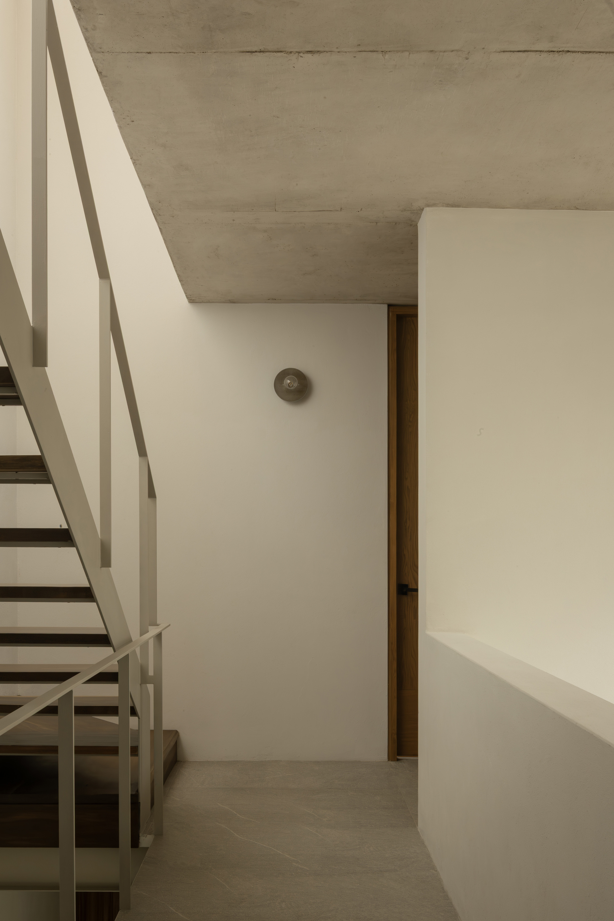 Interior corner showing metal staircase with white railings beneath board-formed concrete ceiling