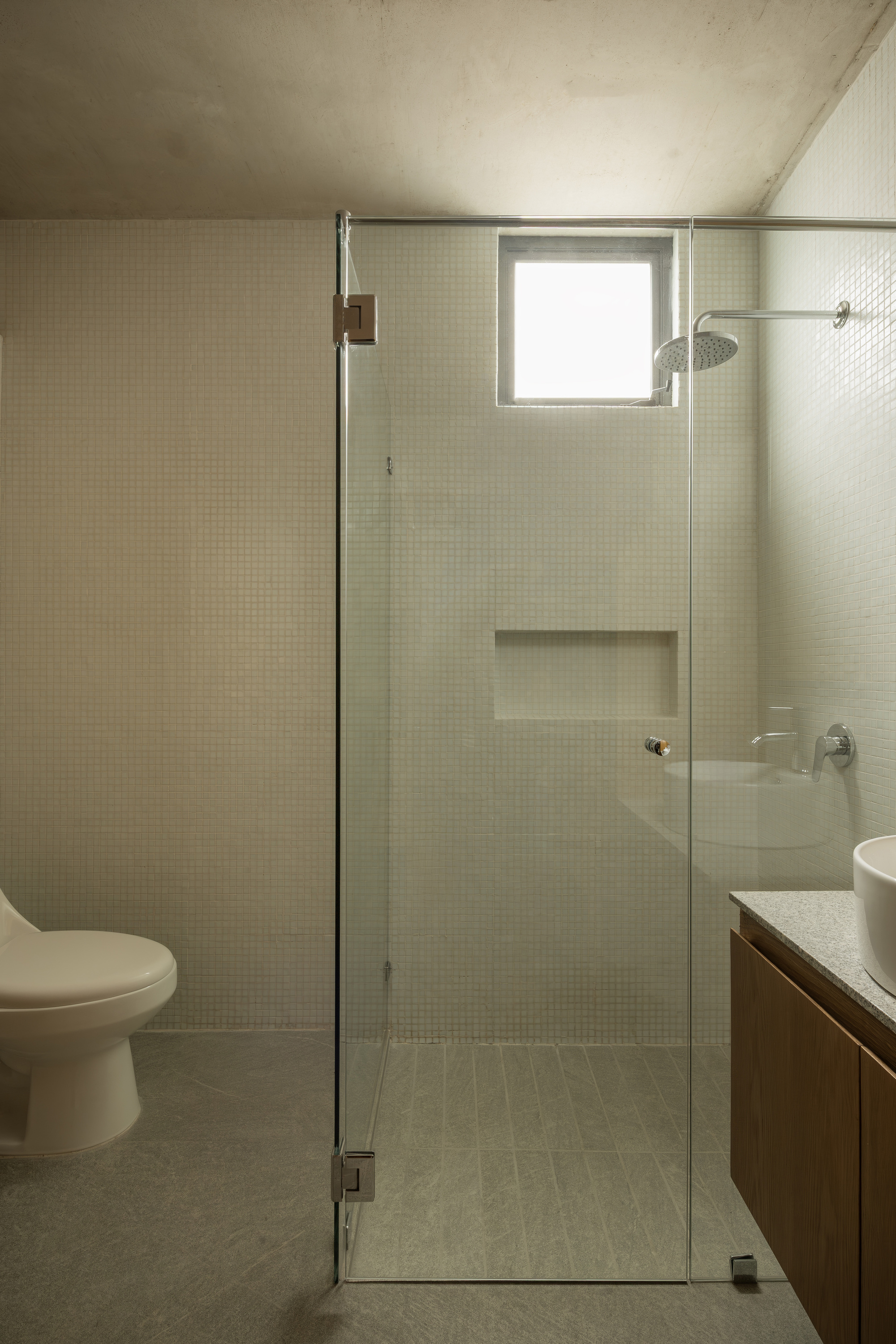 Bathroom with small mosaic tiles, glass shower enclosure and recessed concrete ceiling