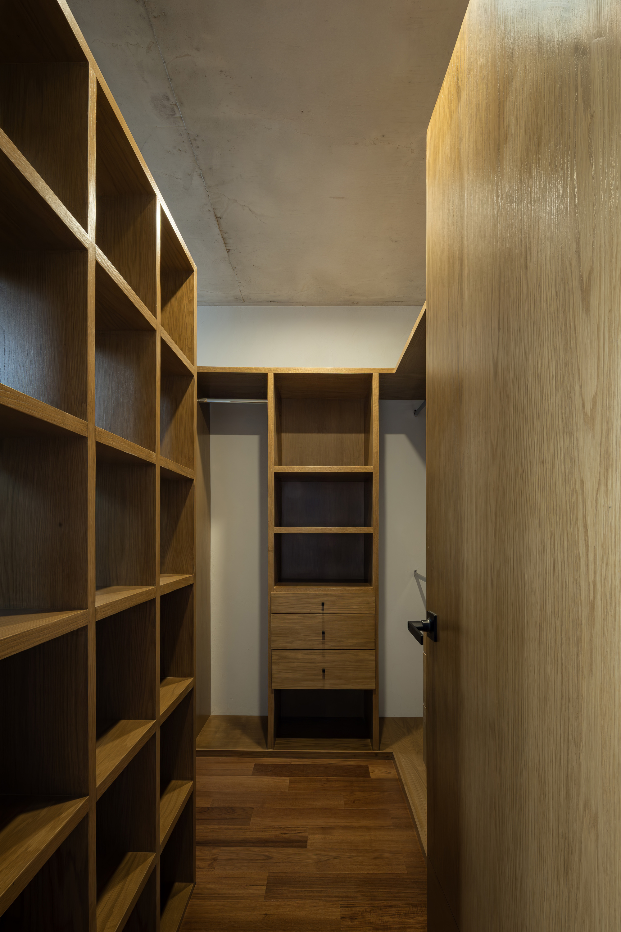 Timber storage corridor with exposed concrete ceiling and concealed lighting above shelving units