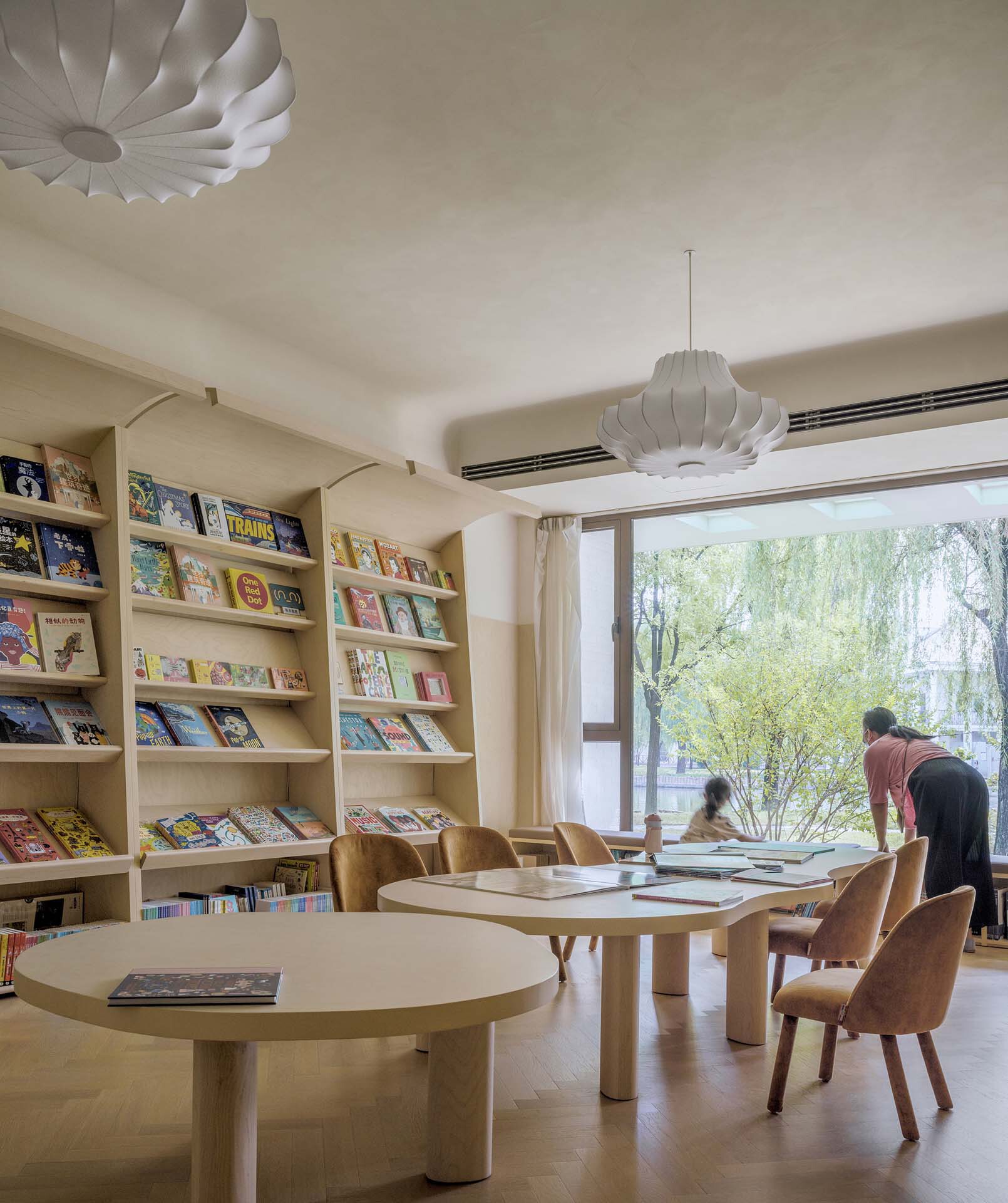 Reading room with built-in bookshelves and round tables beneath pendant lights overlooking the garden