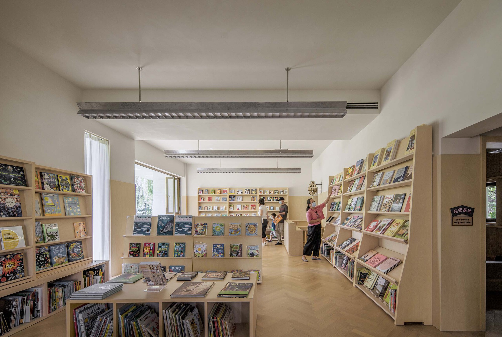 Interior view of library with plywood bookshelves and exposed ceiling beams with visitors browsing books