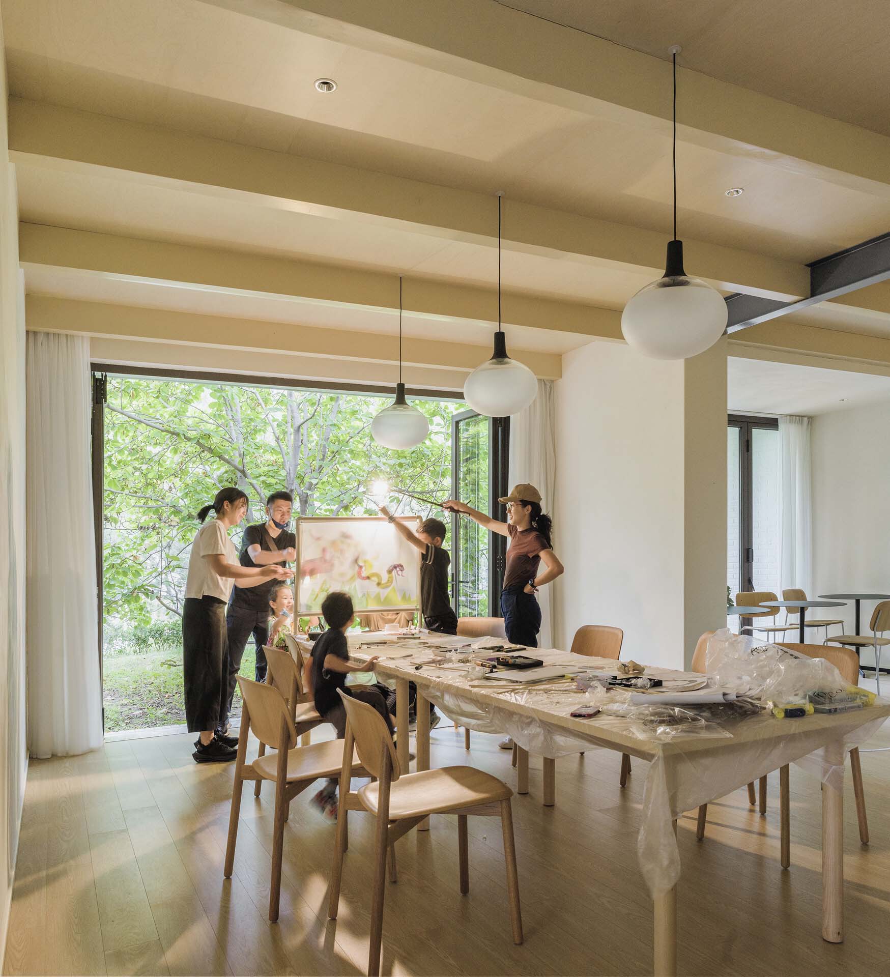 Reading room with timber table and pendant lights where a group gathers for an art workshop