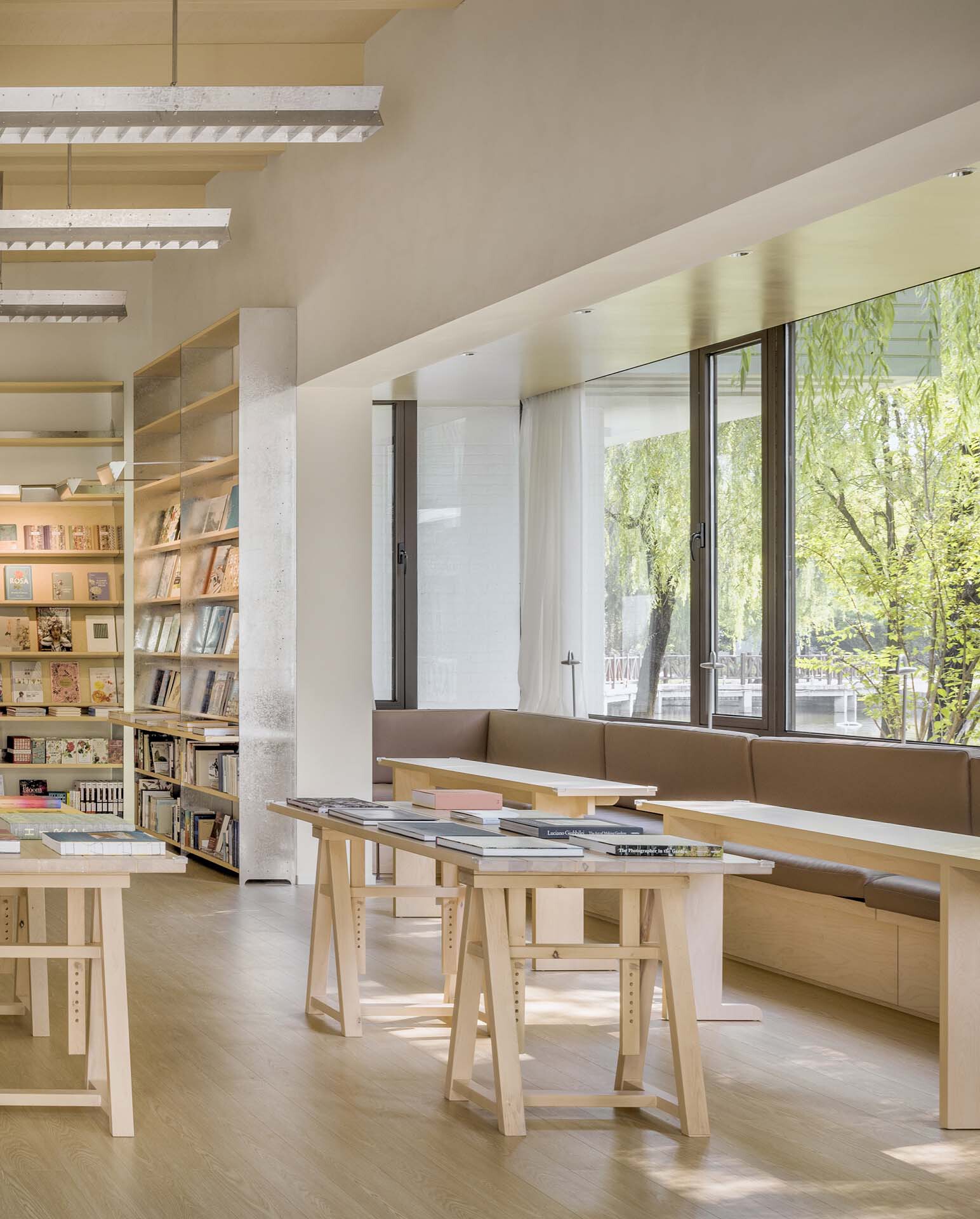 Reading nook with timber display table and built-in bench seat beside full-height windows facing greenery