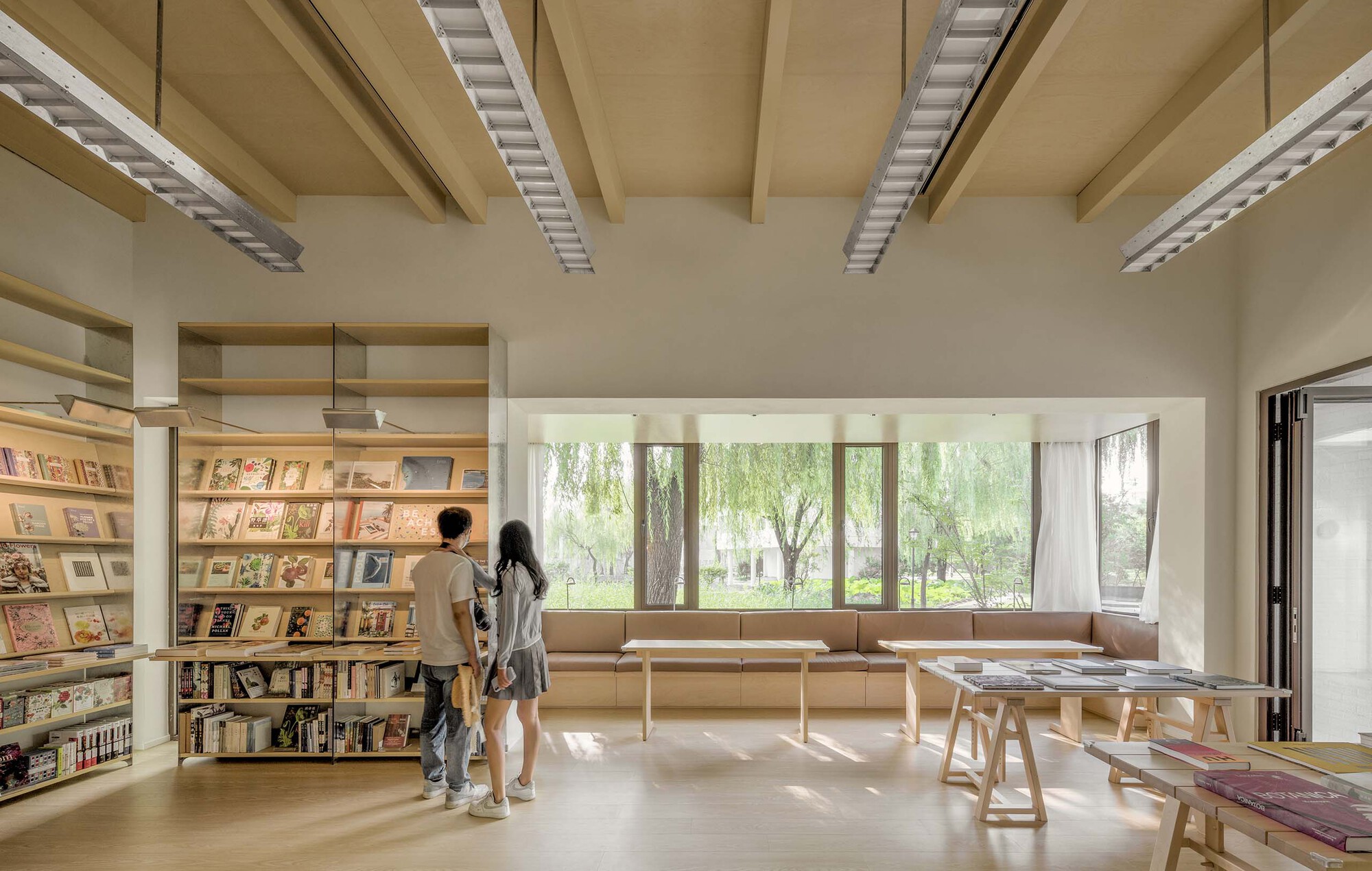 Timber ceiling beams and recessed light slots above a bookshop reading room with visitors browsing near the windows