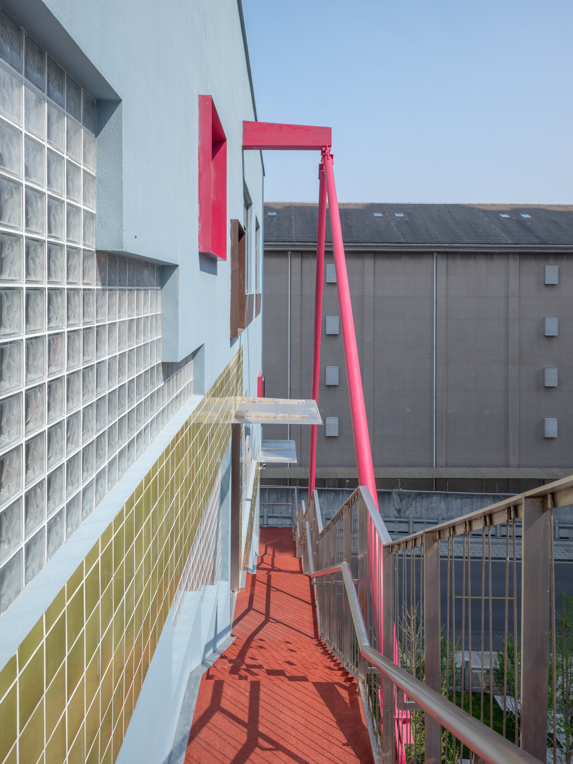 Elevated pink steel pedestrian bridge with glass block wall on one side under overcast sky