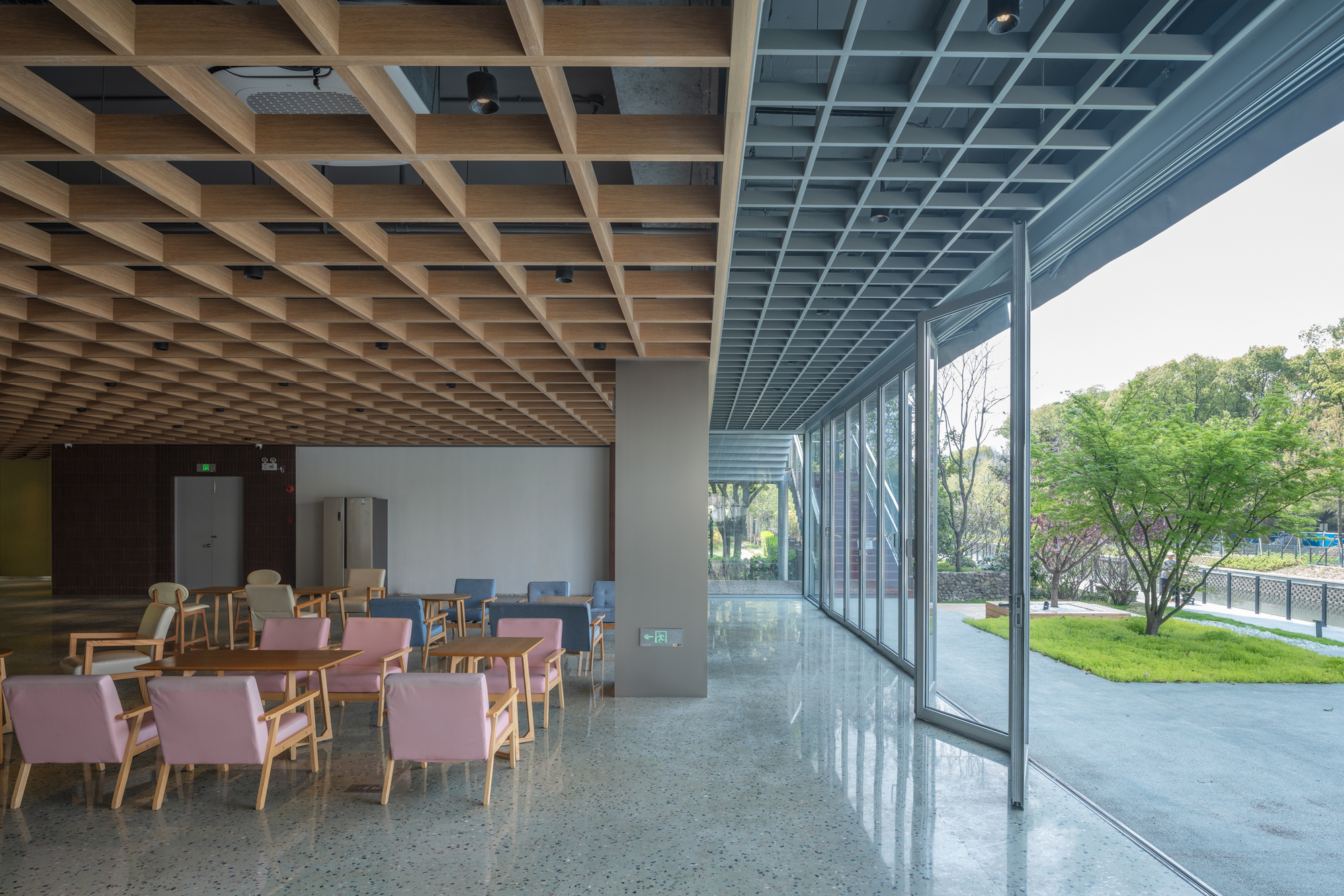 Interior dining area with timber grid ceiling and floor-to-ceiling glass wall overlooking green landscape