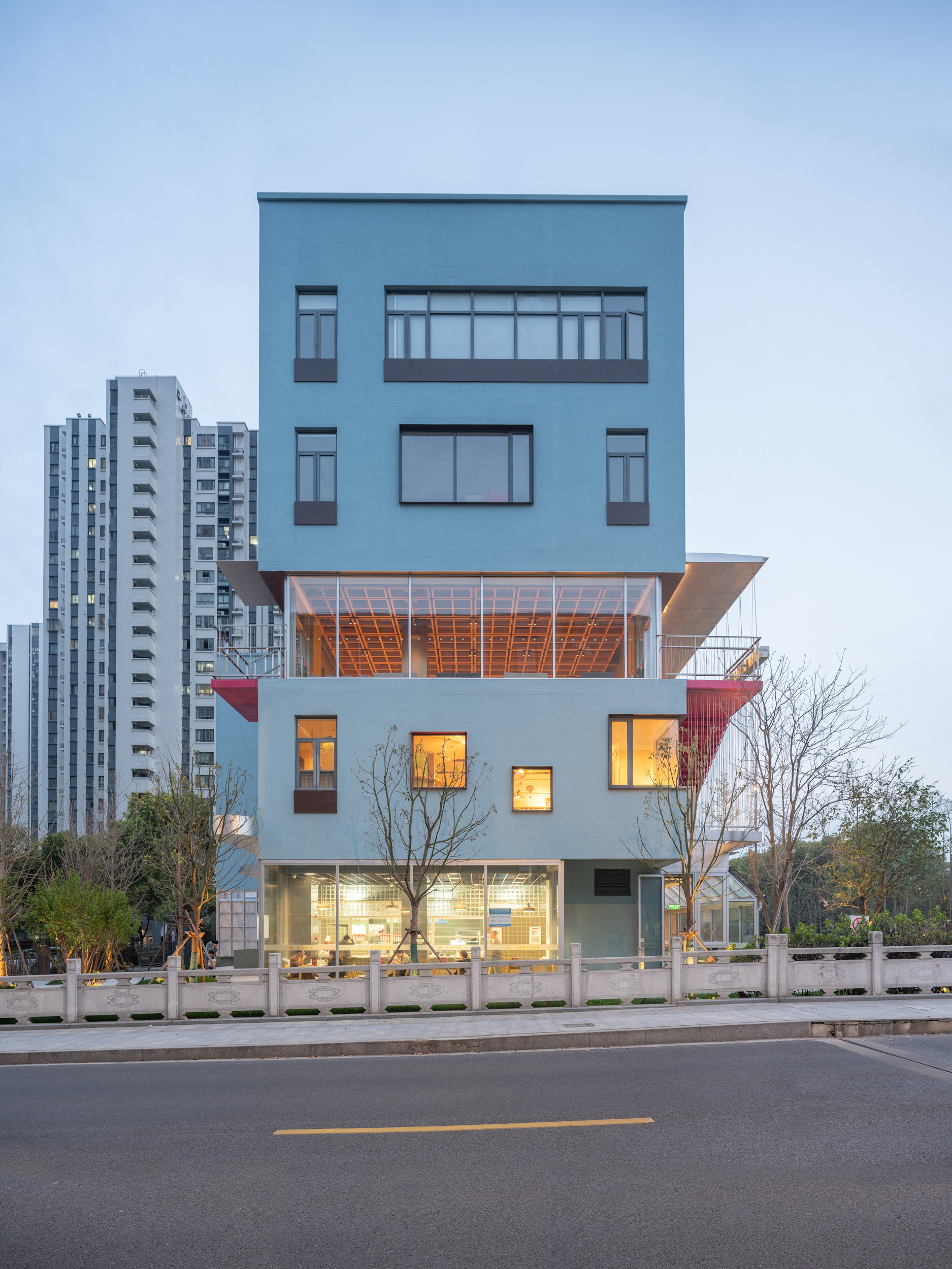 Five-storey facade with cantilevered timber-clad volume and illuminated interior at twilight