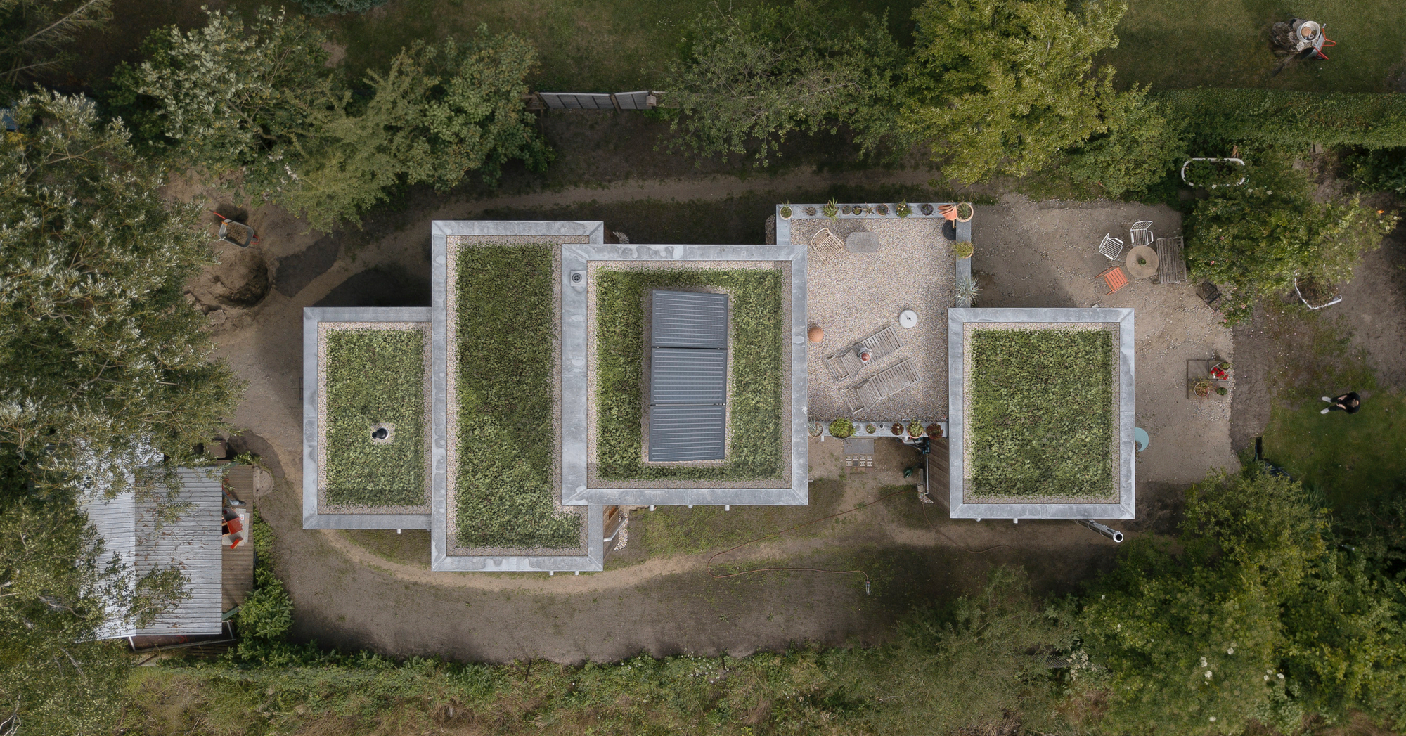 Aerial view of three grass-covered roof volumes with white parapets and a central skylight