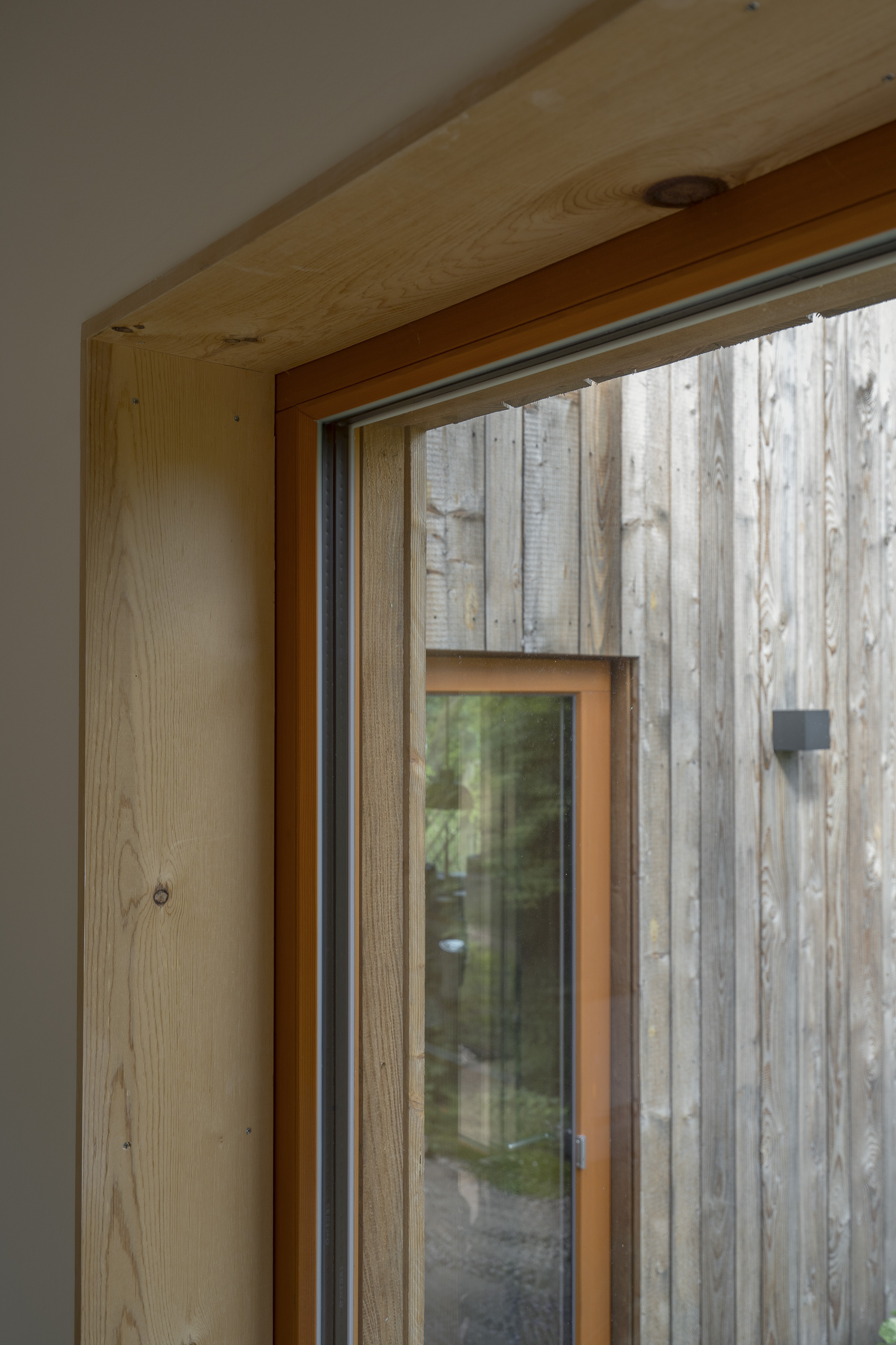 Interior view of timber window jamb and soffit framing the weathered vertical timber cladding outside