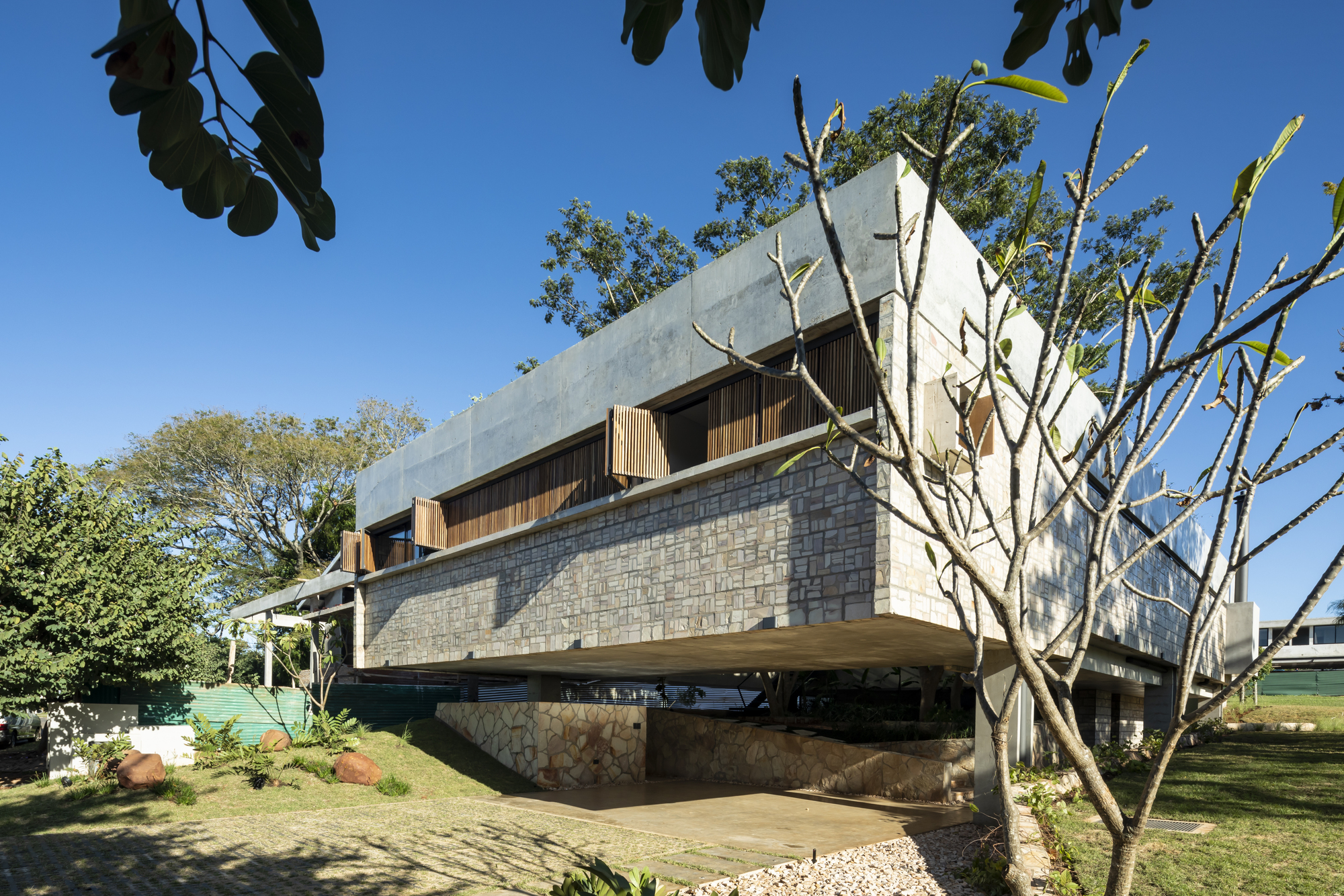 Cantilevered structure supported by concrete pillars with stone cladding and bare trees in foreground