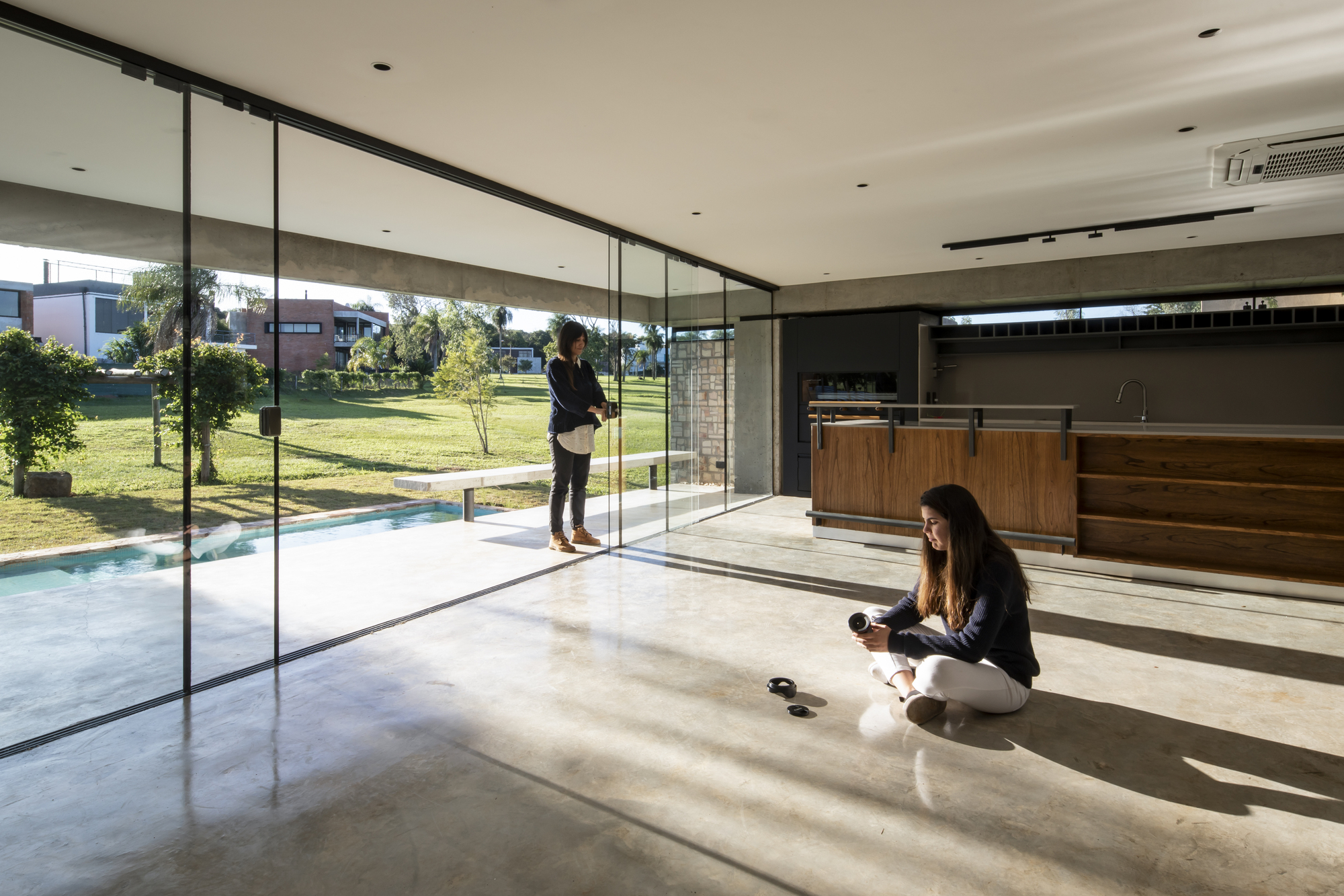 Open-plan kitchen and living area with floor-to-ceiling glass overlooking lawn with two people inside