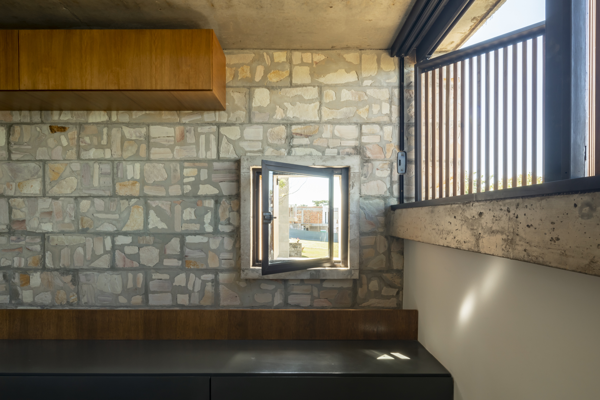 Stone wall with small deep-set window and wooden range hood above dark countertop