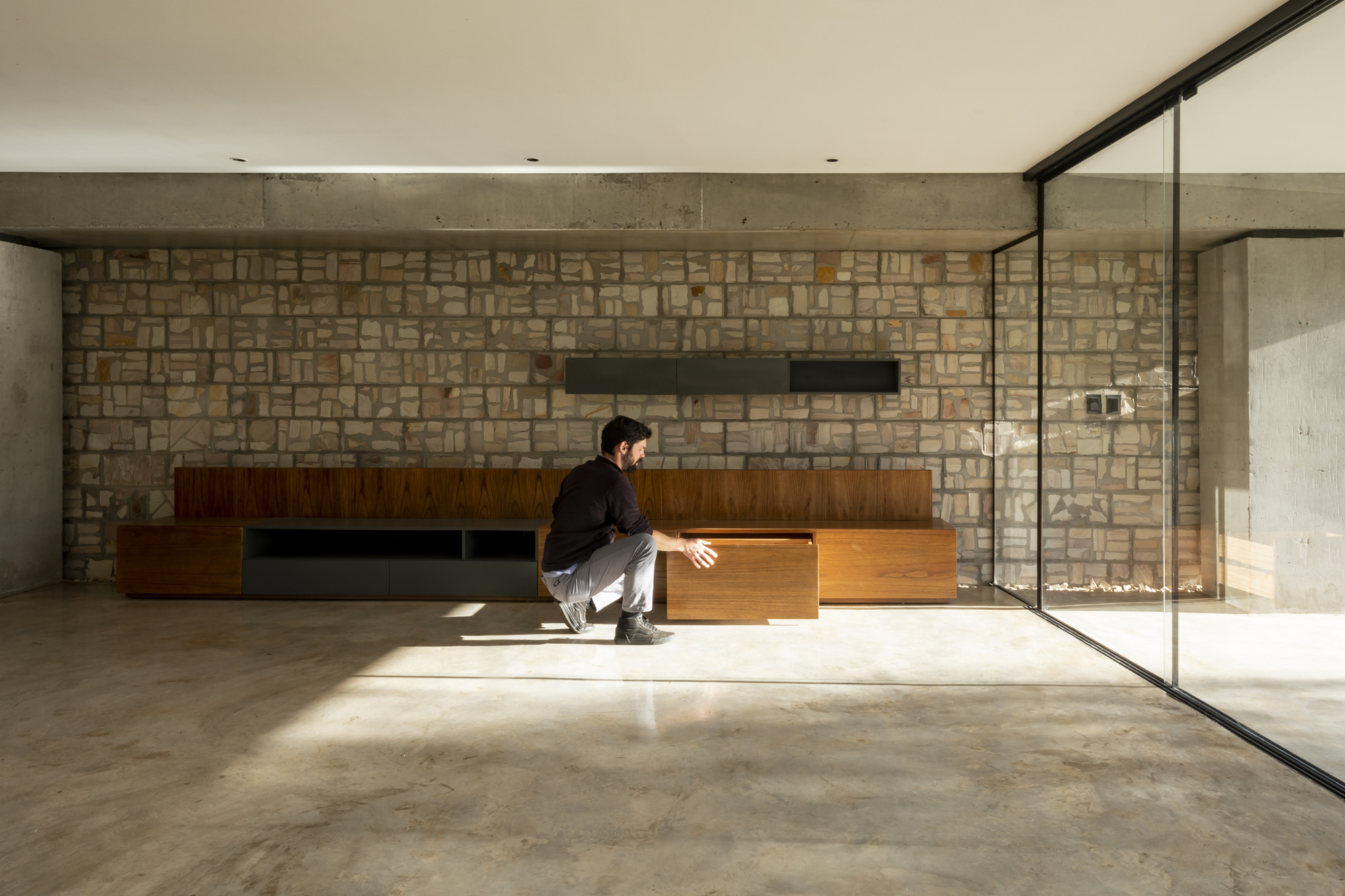 Living space with concrete ceiling and stone wall where a person sits in sunlight