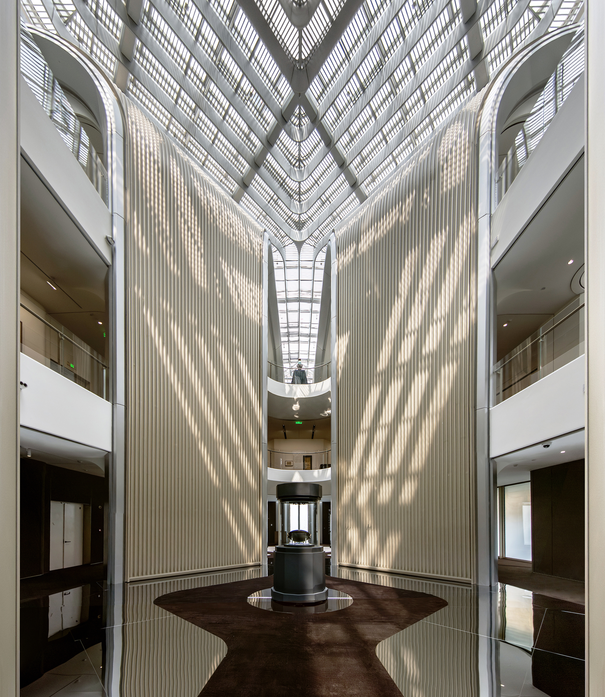 Central atrium looking upward showing vertical ribbed walls and a diamond-patterned skylight with dappled sunlight