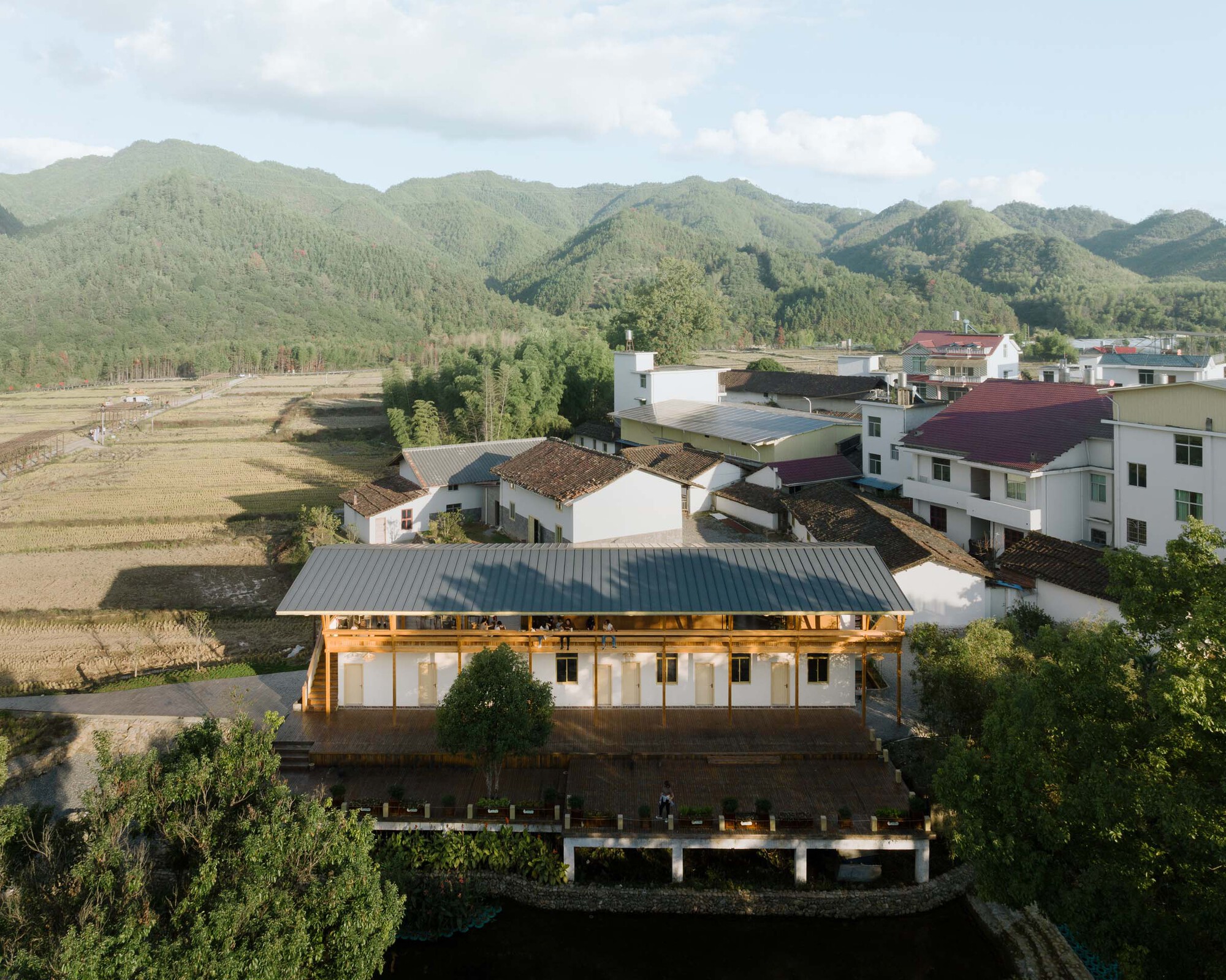 Aerial view of the white-rendered building with metal roof surrounded by rice fields and village houses