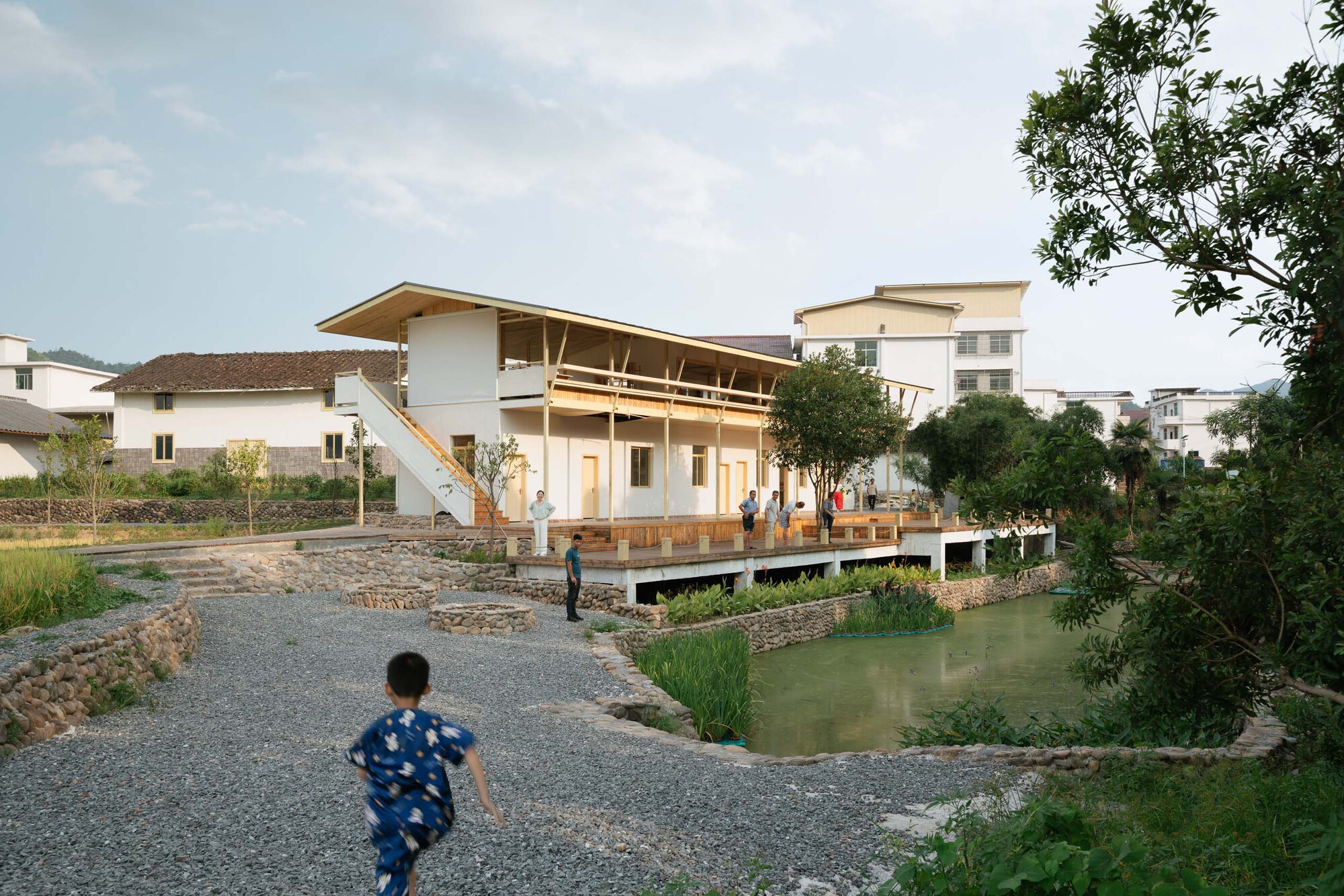 Terrace and retention pond with gravel pathway as a child runs toward the building entrance