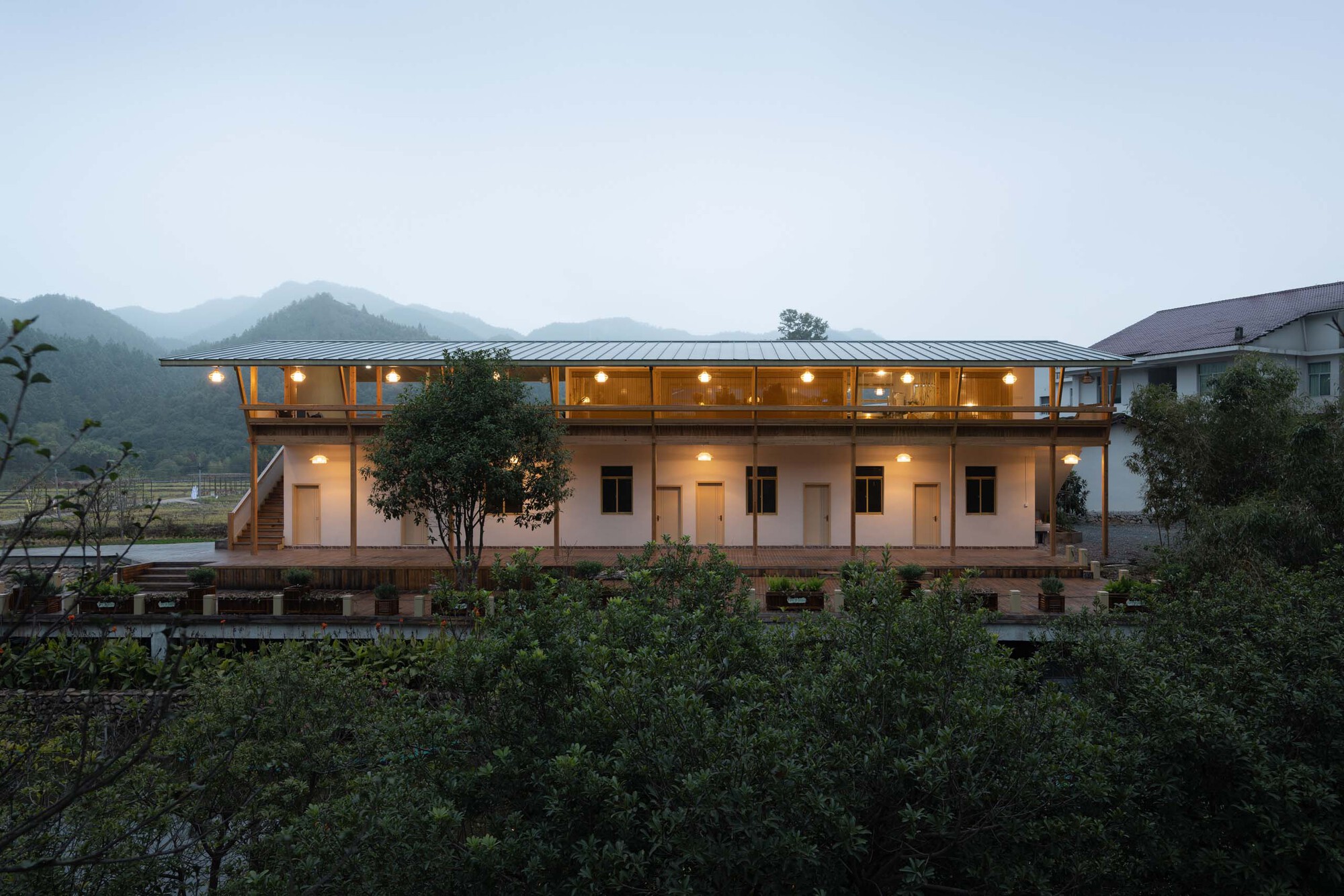 Long elevation showing the white ground floor with strip windows and glowing timber upper level at twilight