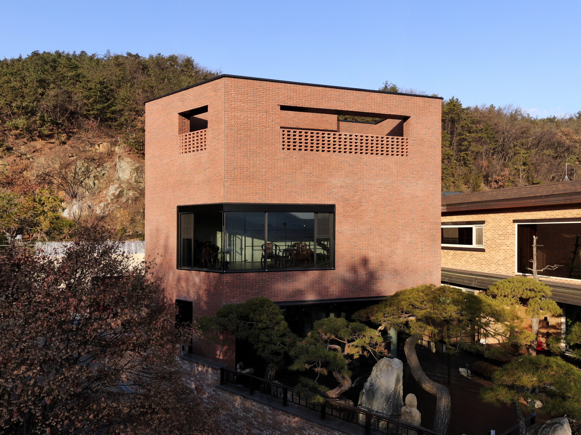 Red brick facade with perforated rooftop parapet and horizontal window band in late afternoon sunlight