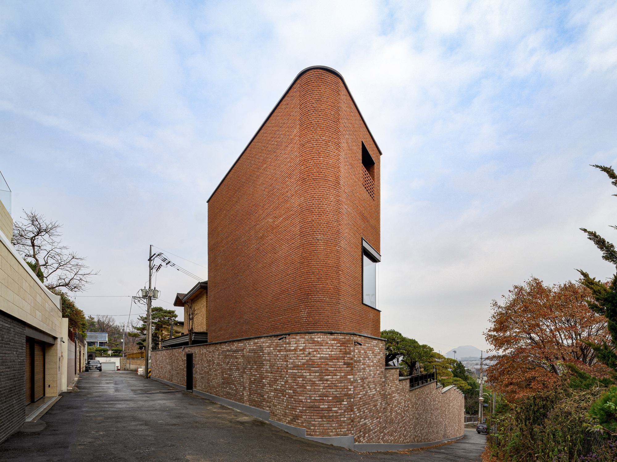 Cylindrical brick tower rising from a curved base wall along a sloped residential street