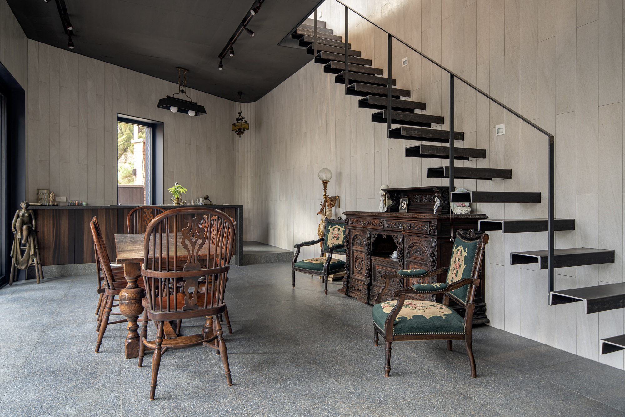 Floating black steel staircase ascending against a white paneled wall in a double-height dining area