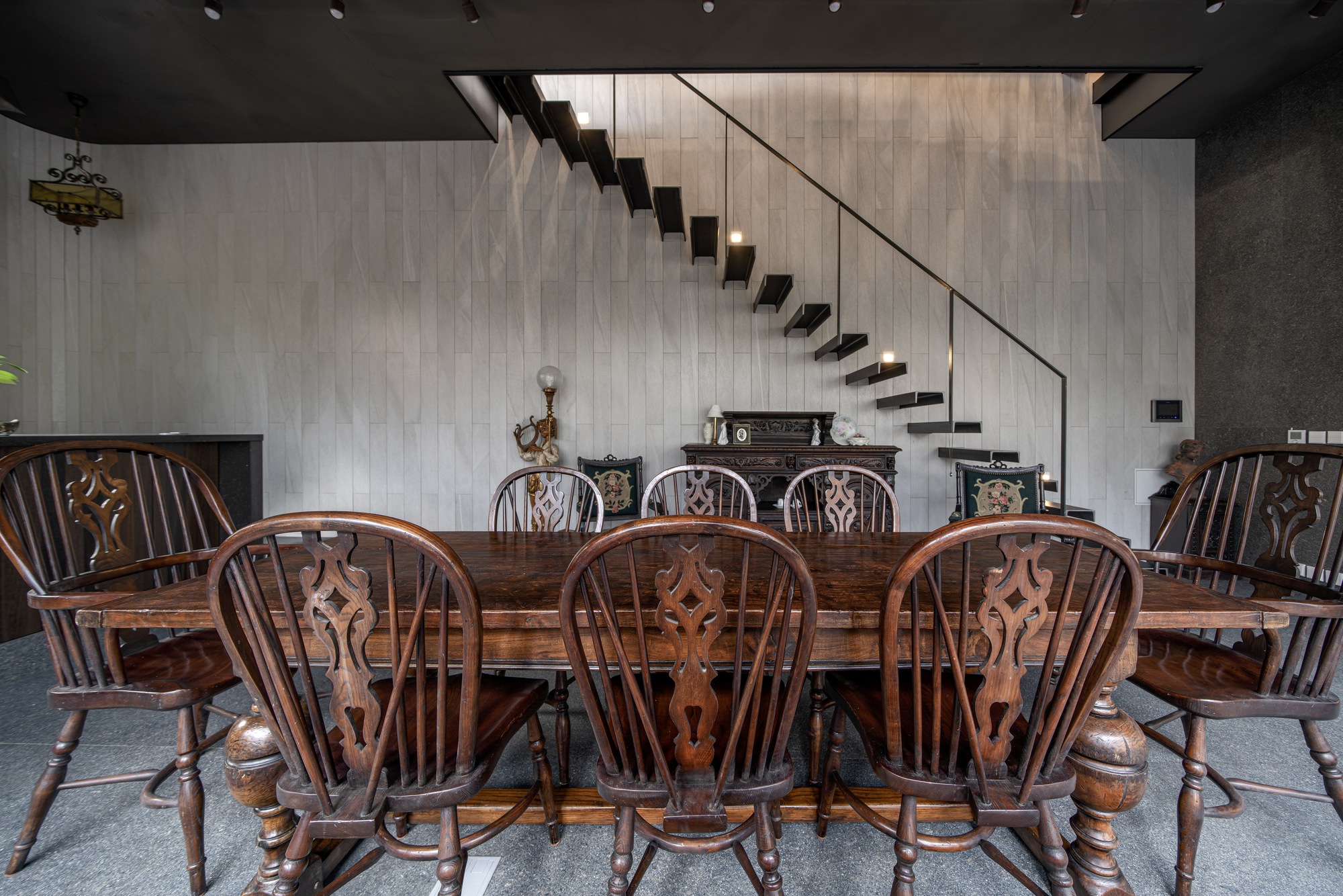 Carved wooden dining chairs arranged around a long table beneath the cantilevered black steel stair
