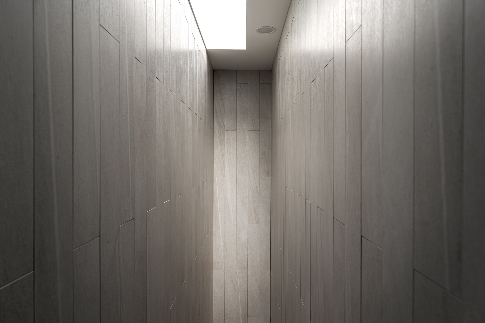 Narrow corridor lined with pale timber paneling and illuminated by a skylight overhead