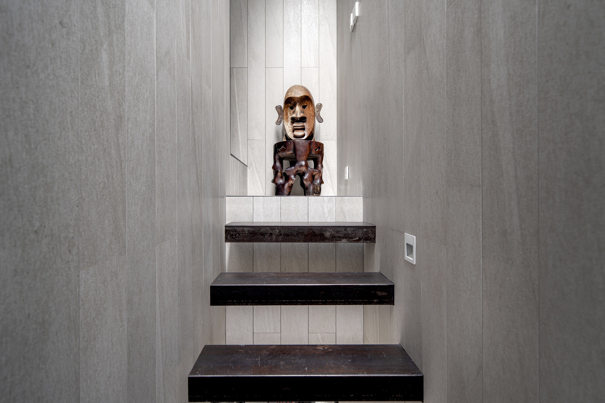 Stairwell with dark cantilevered treads and pale timber wall panels framing a carved mask