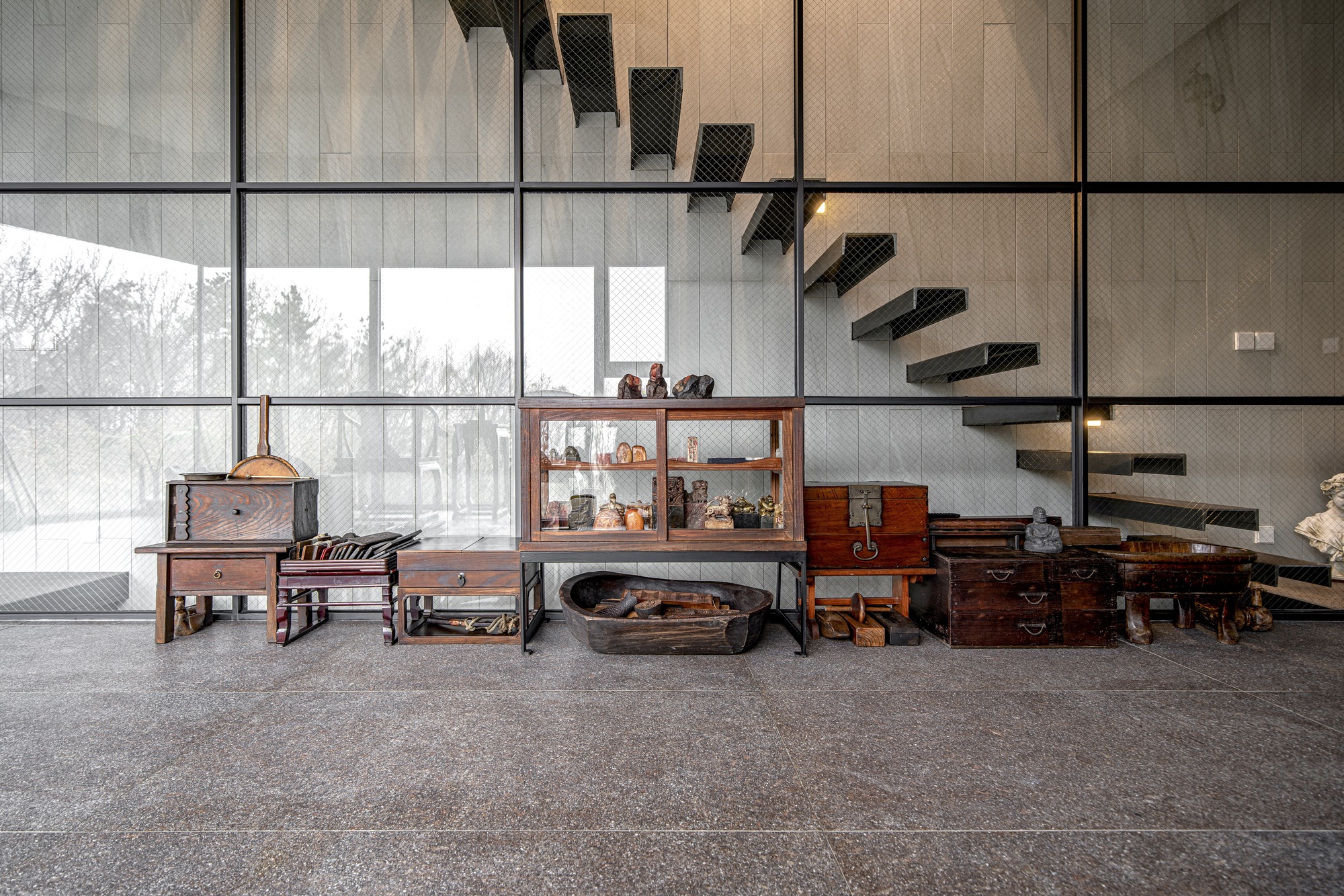 Floating black steel staircase alongside floor-to-ceiling gridded windows framing bare winter trees