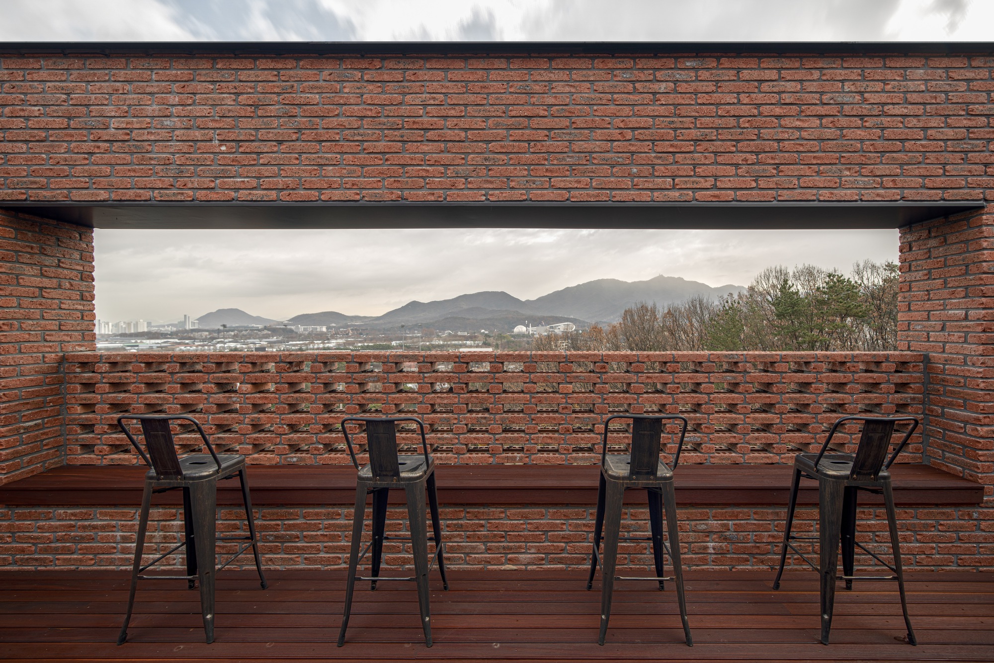 Rooftop terrace with timber decking and perforated brick parapet overlooking distant mountains at dusk