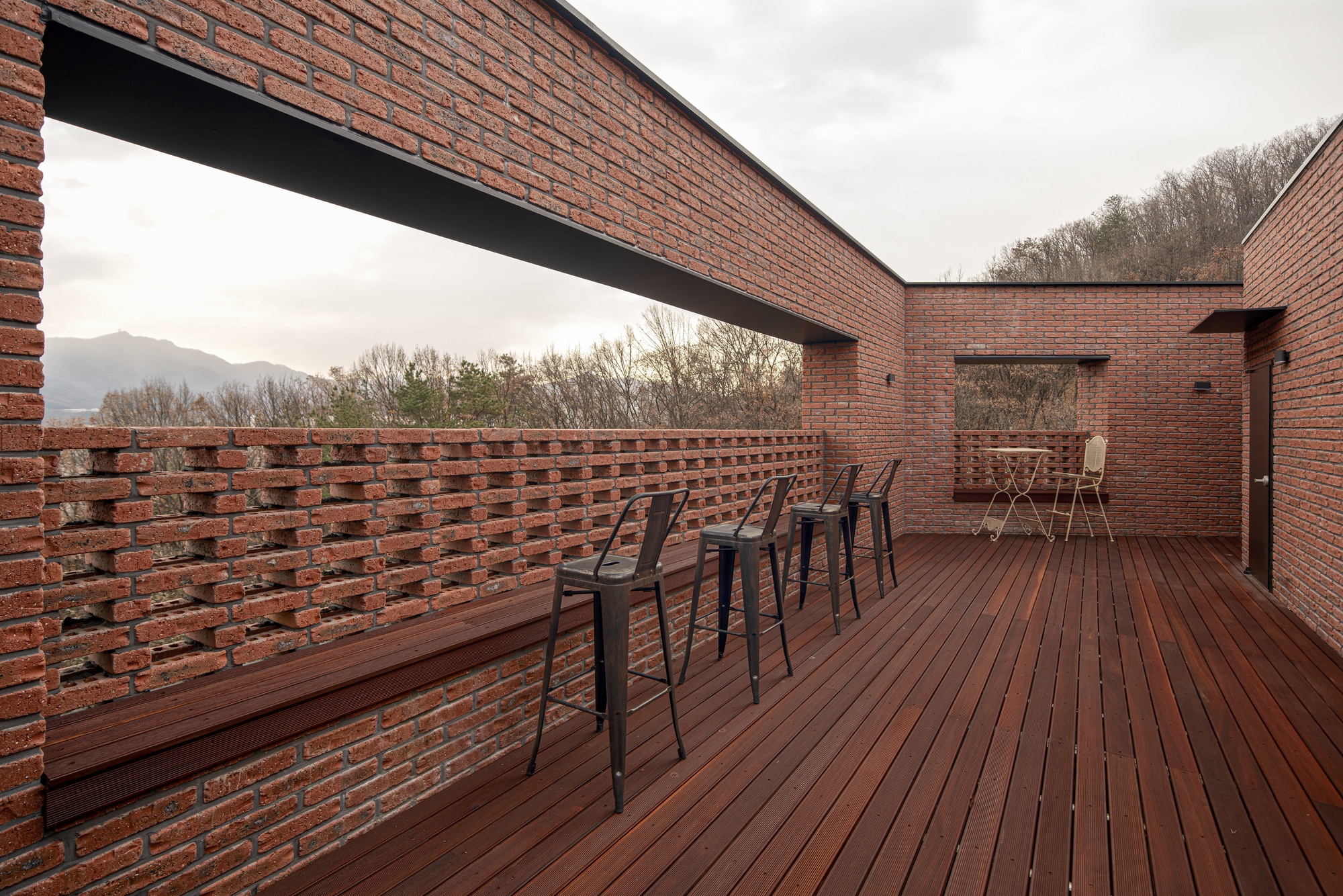 Rooftop terrace with perforated brick parapet wall and timber decking under an overcast sky