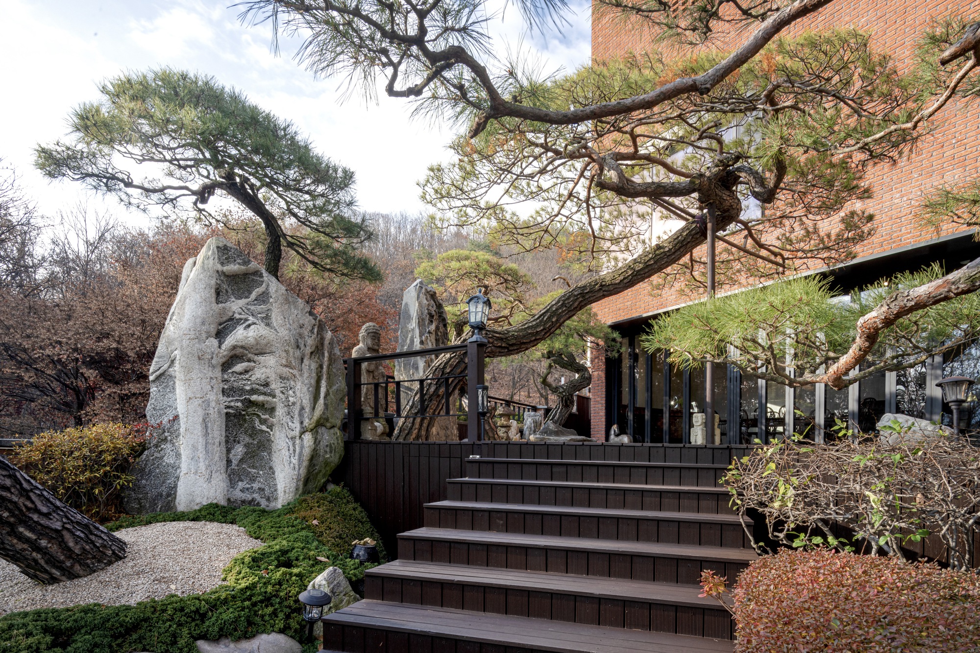 Wide timber staircase ascending past weathered rocks and pine trees toward a brick pavilion