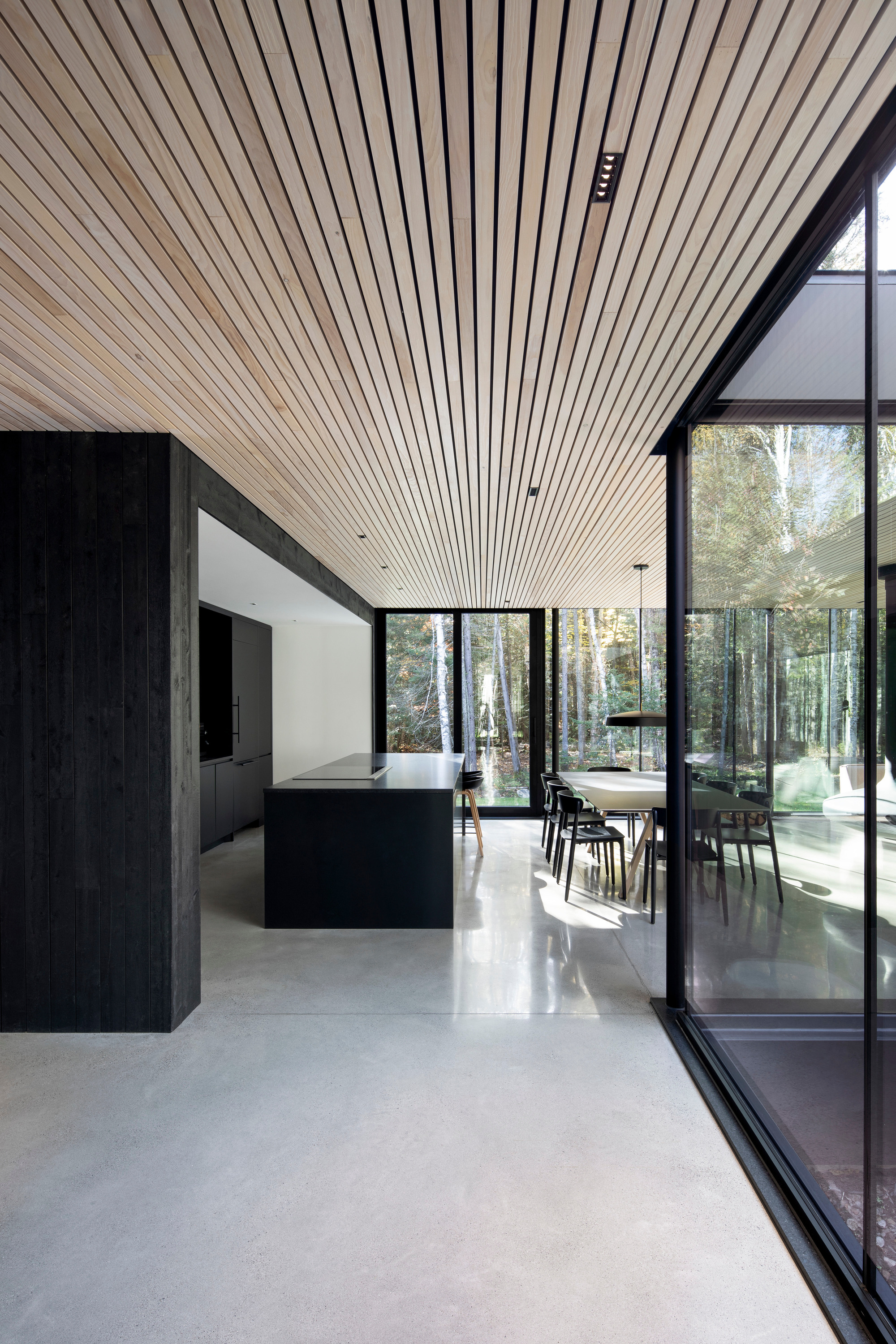 Open kitchen and dining area with wood slat ceiling and polished concrete floor beneath full-height glazing