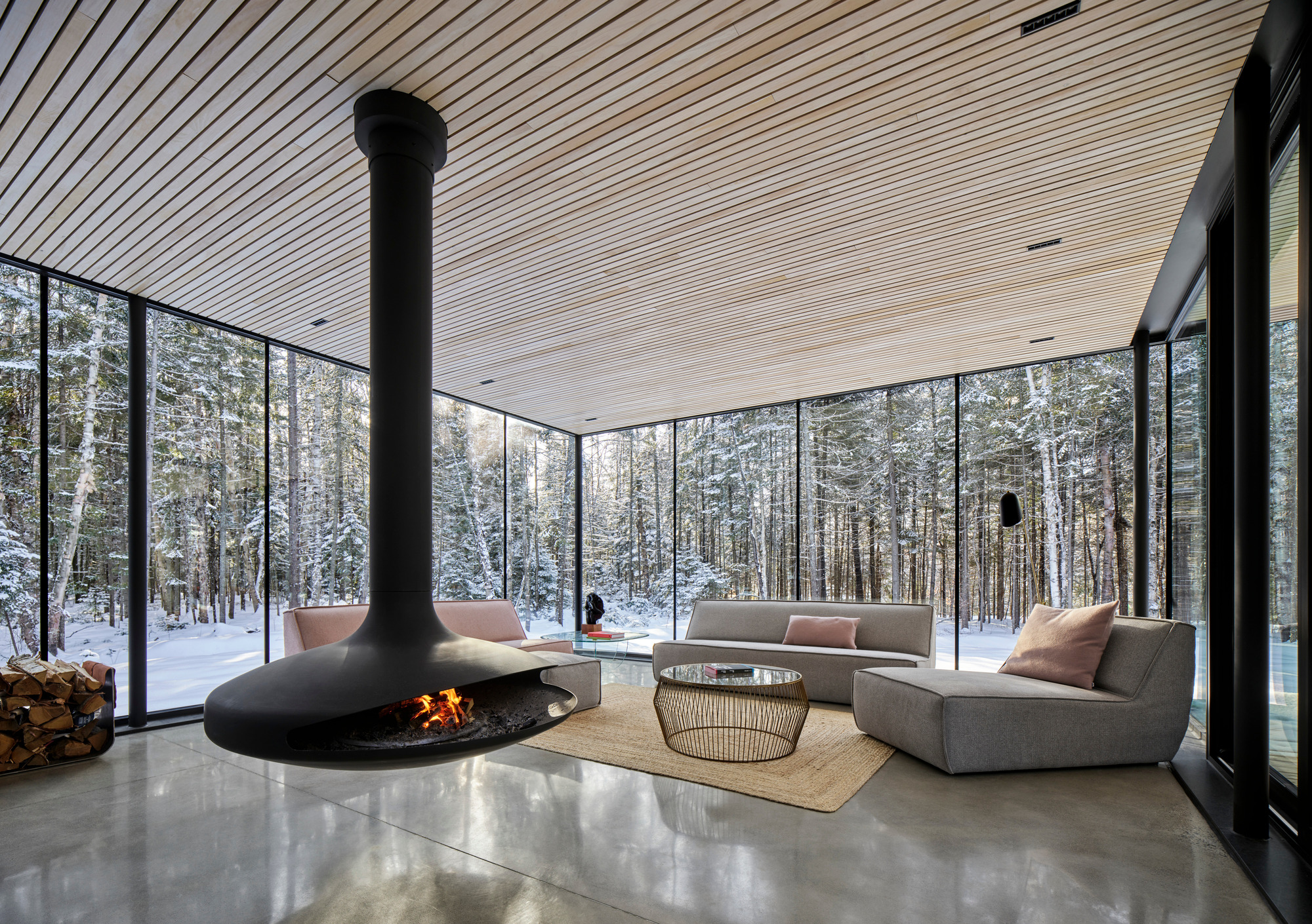 Living area with suspended conical fireplace and floor-to-ceiling glazing overlooking snow-covered forest