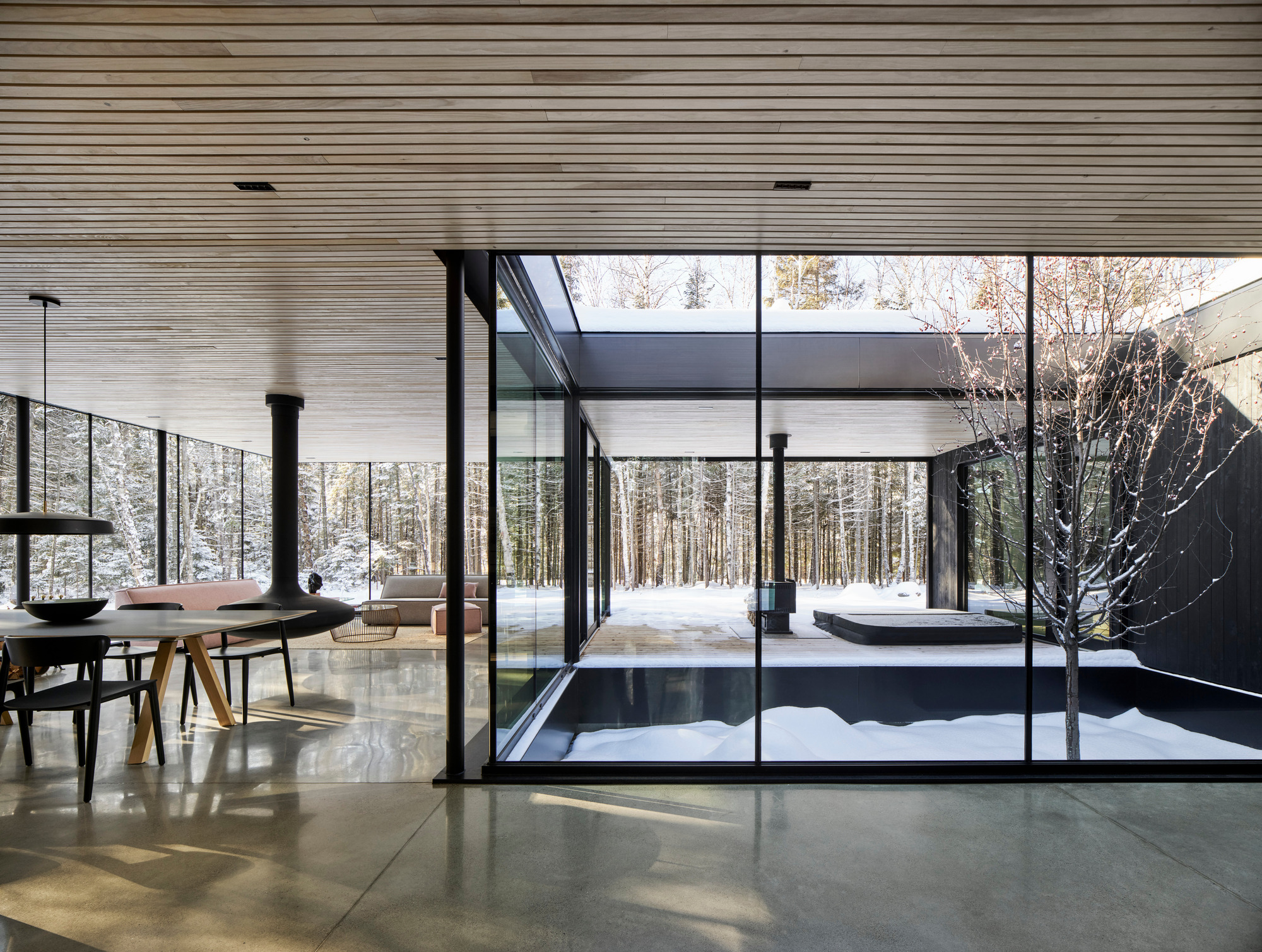 Interior view through black-framed glazing toward central courtyard with tree and snow beyond
