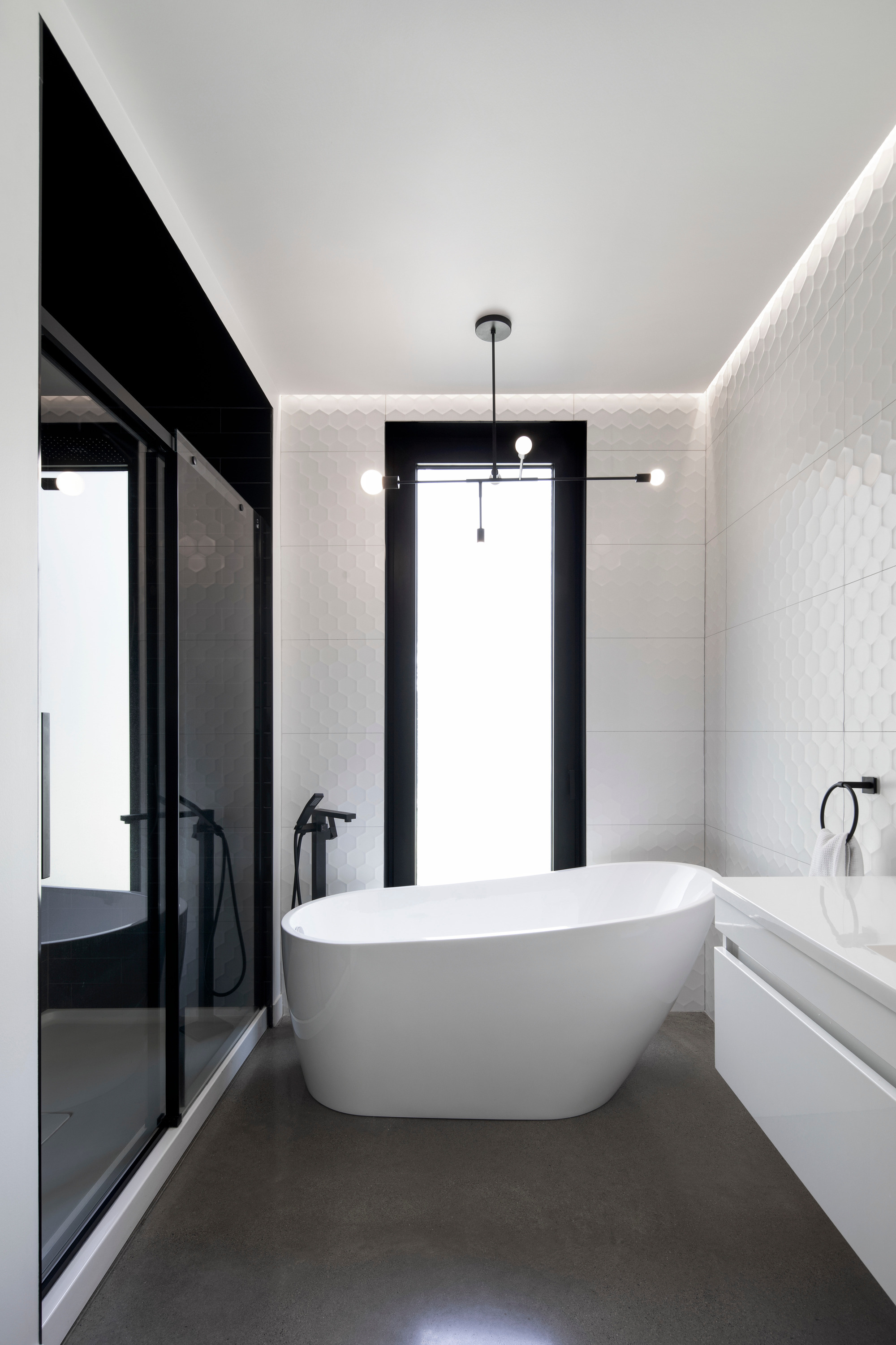 Bathroom with freestanding white tub and concealed perimeter lighting along white tiled walls