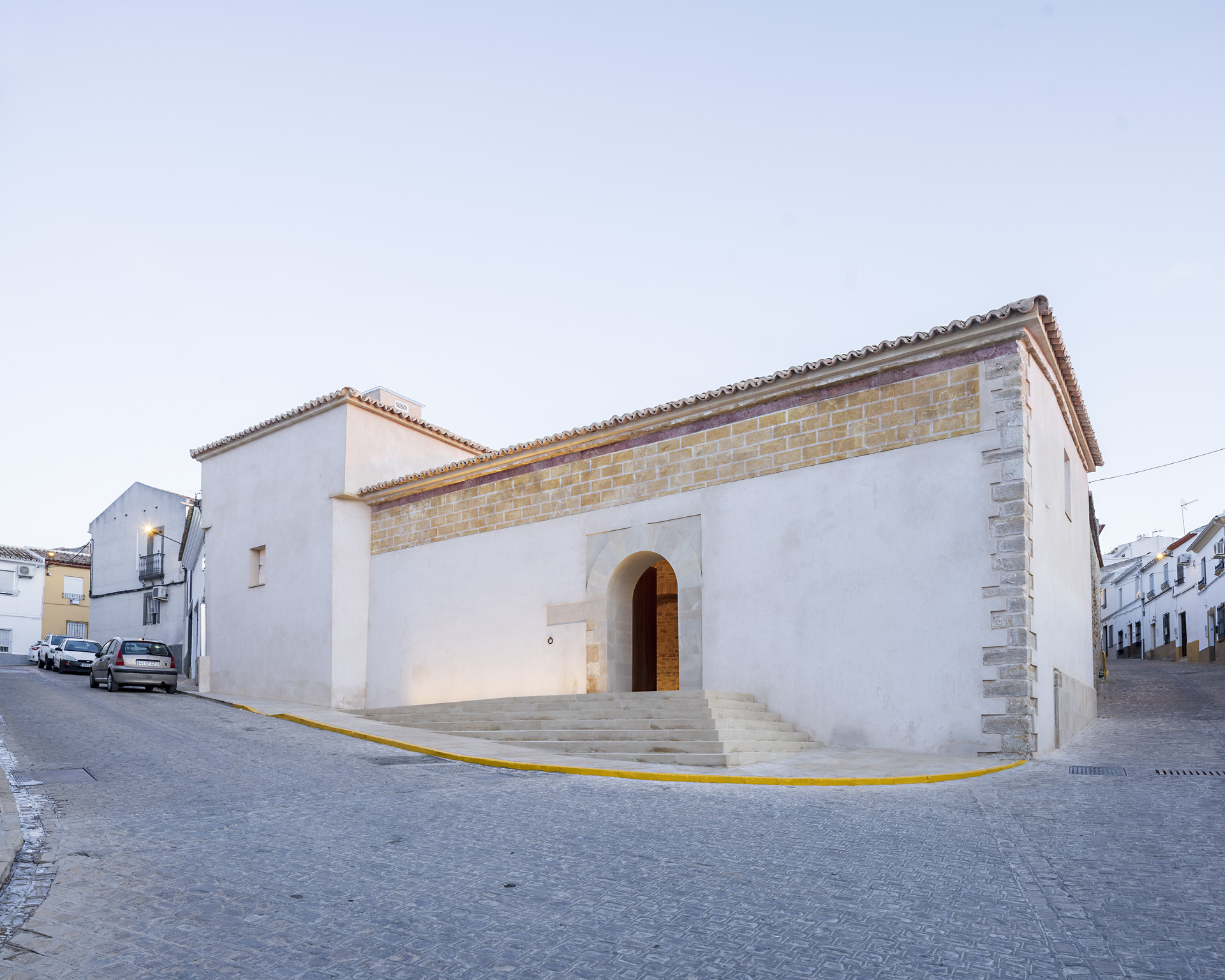Street corner view of the white stucco facade with arched entry and terra cotta tile roof at dusk