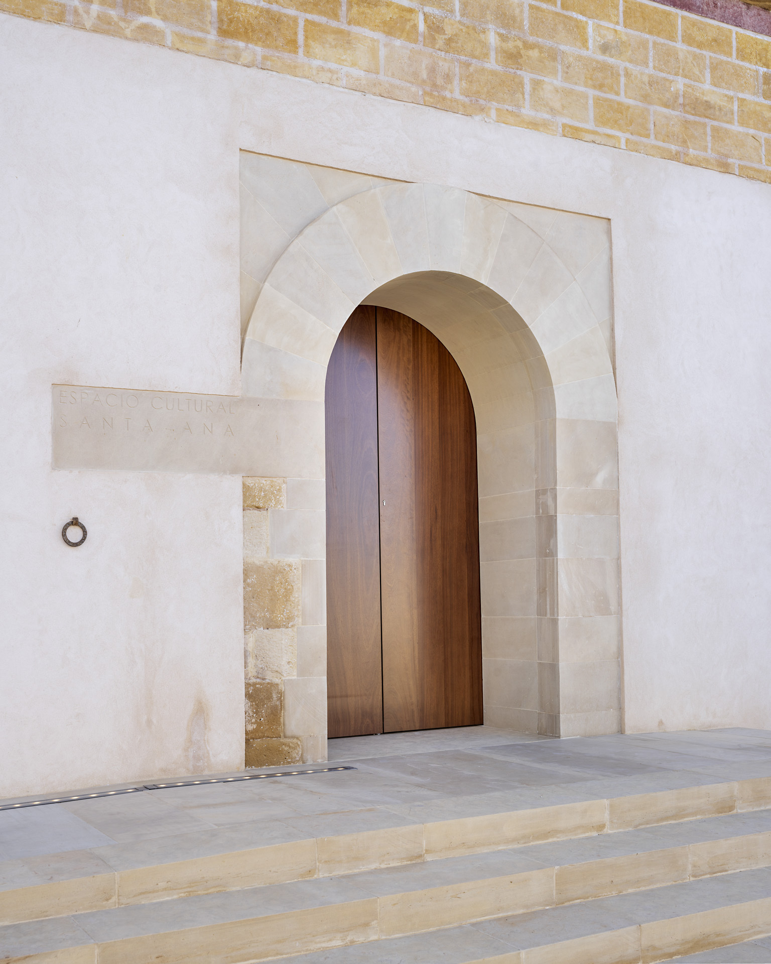 Arched timber entry door framed by limestone voussoirs set within a white stucco facade above stone steps