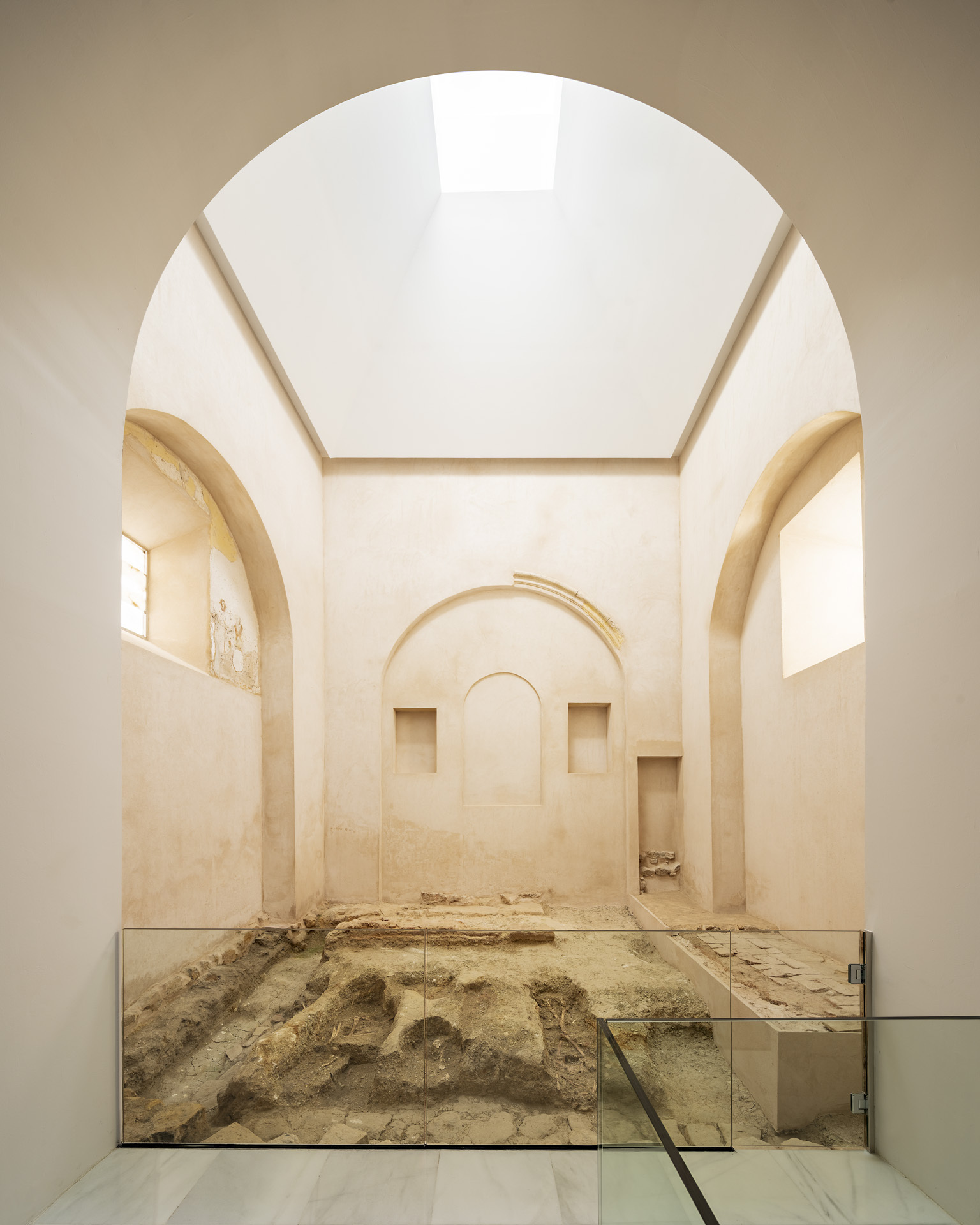 Vaulted room with central skylight above archaeological excavation site framed by arched niches