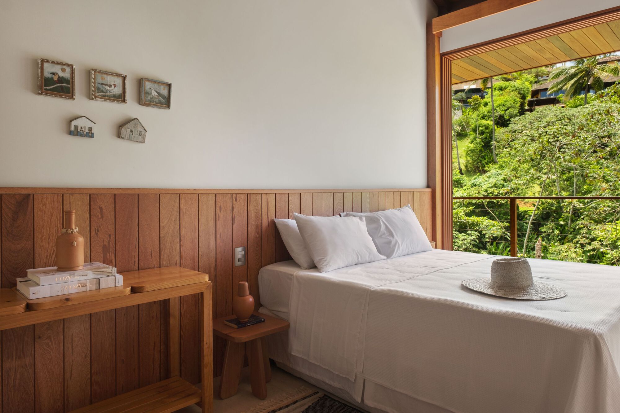 Bedroom with vertical timber paneling and large opening framing vegetation outside