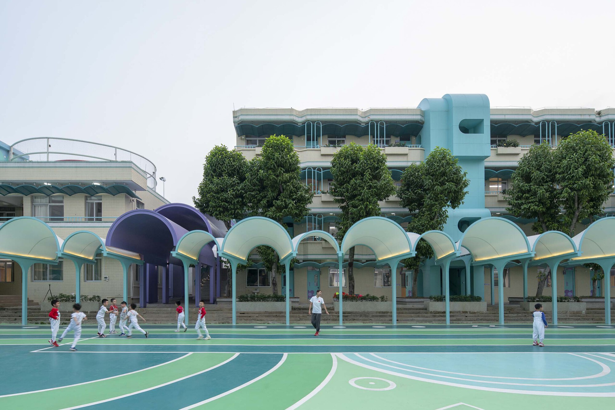 Row of arched canopies in pastel blue and purple shades sheltering a playground with children playing