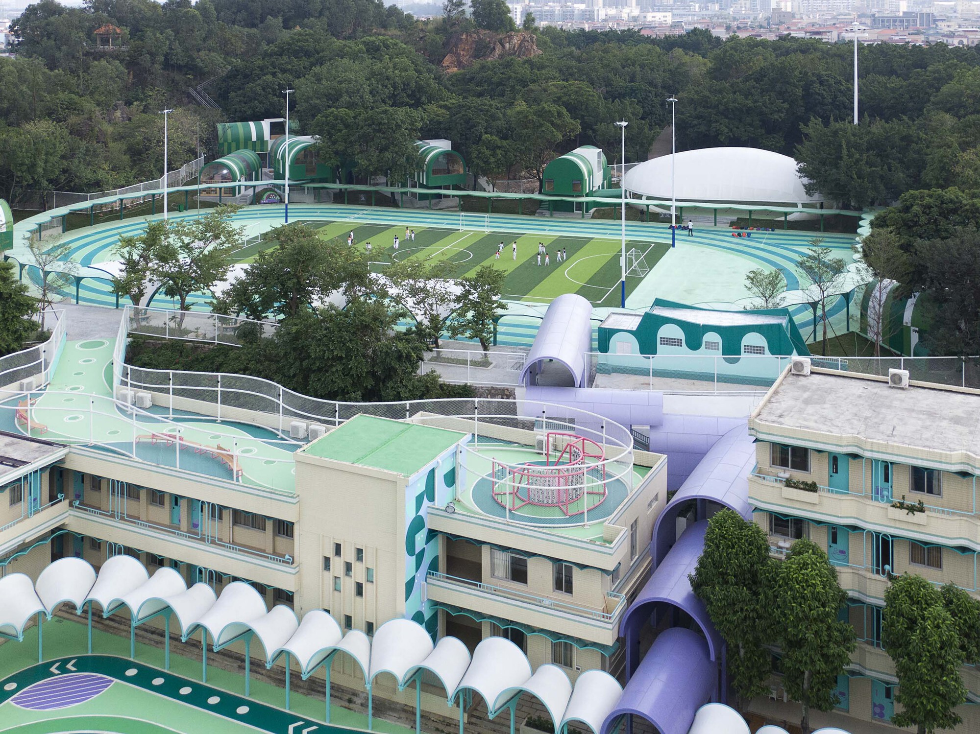 Aerial view of the terraced campus with curved running track and domed canopies among tree canopies