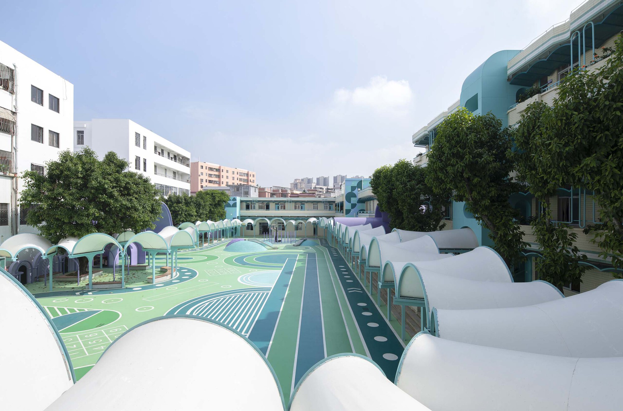 View across the painted playground surface toward rows of white and purple shell-like canopies under cloudy skies